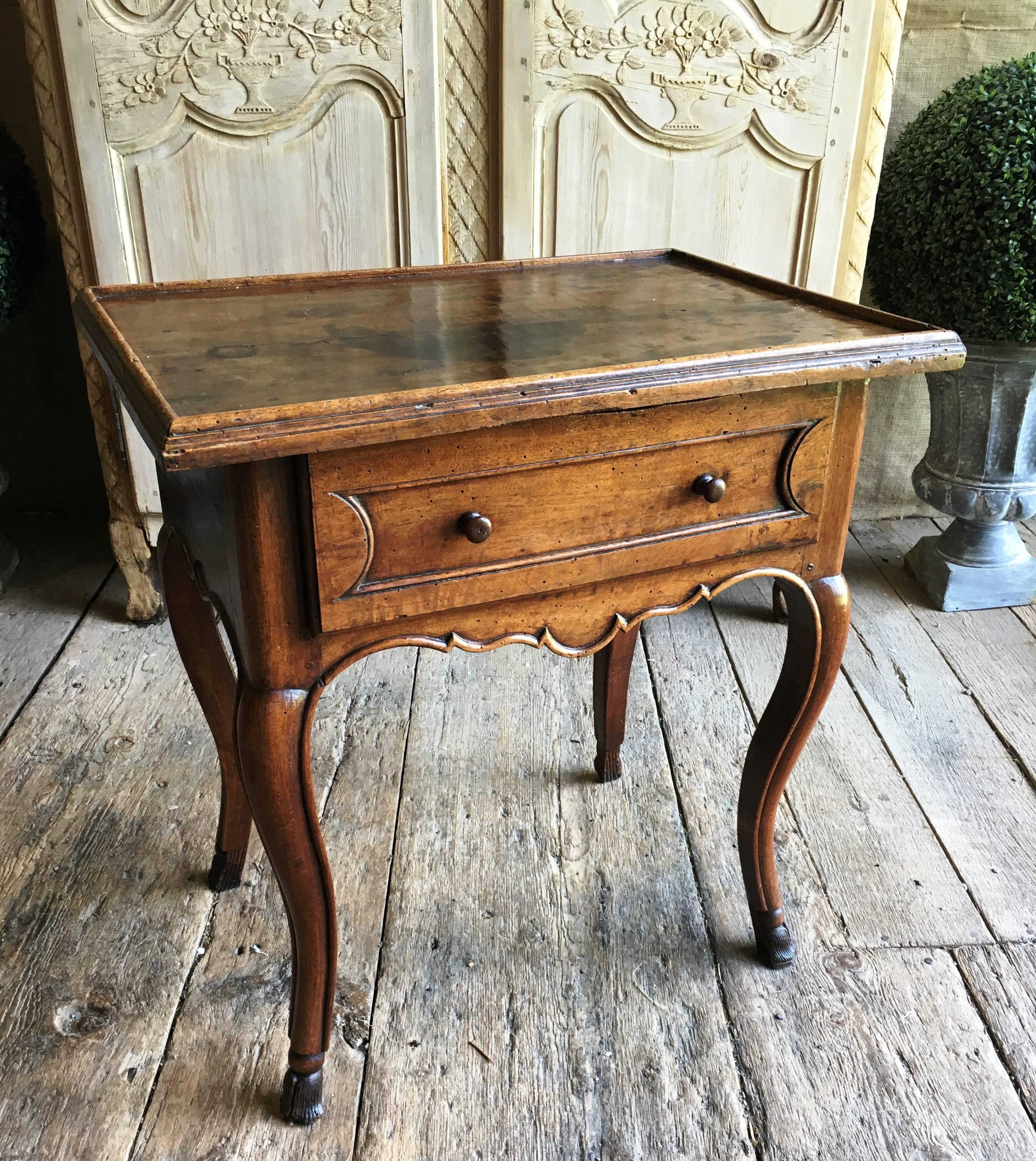 A Louis XV period side table from Provence with a single drawer, a scalloped apron on cabriole legs with hairy paw feet, in walnut, circa 1760. Original wood pulls on drawer. From the Estate of Ambassador Joseph Verner Reed.