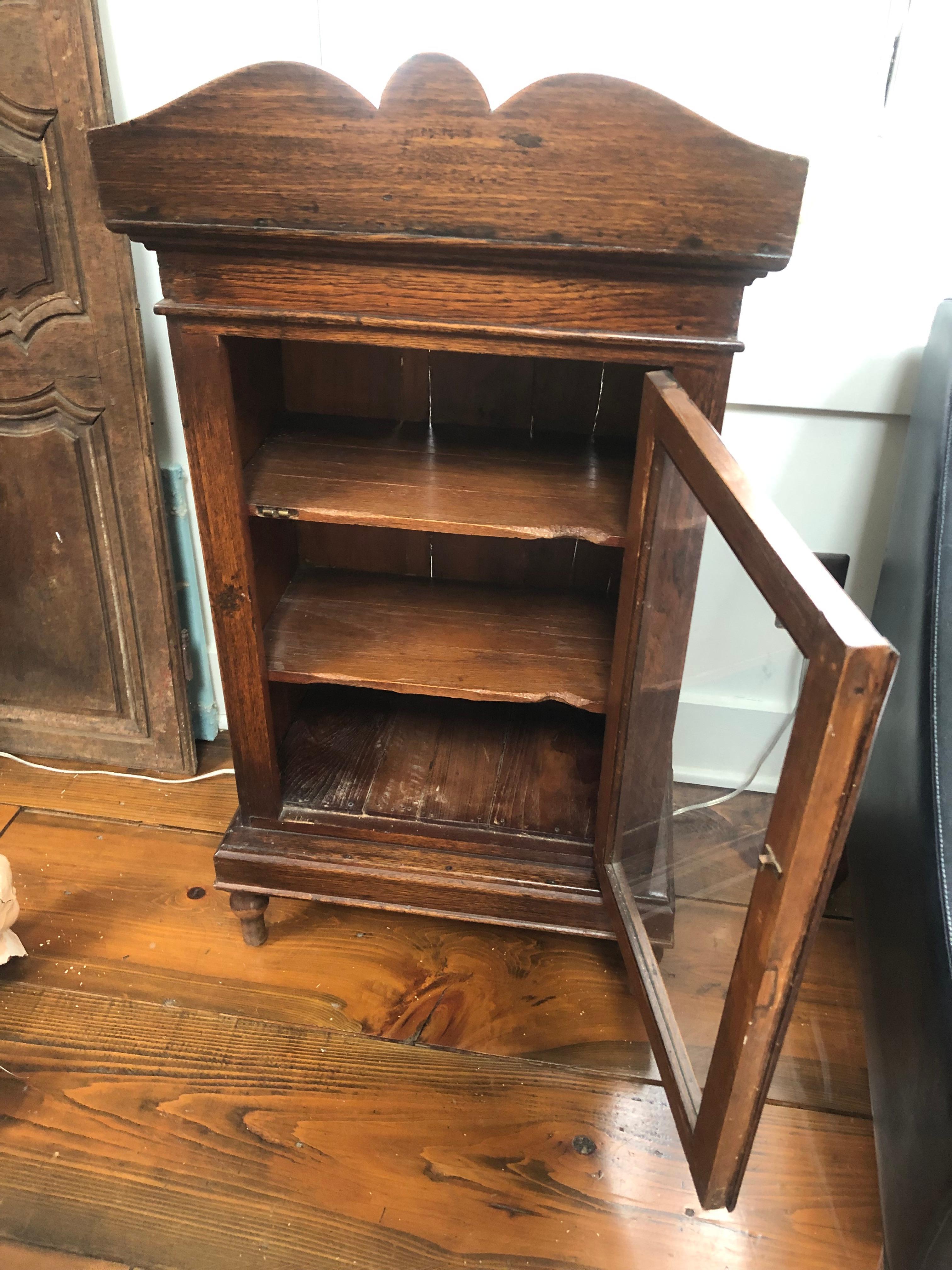 A charming medium sized antique mahogany curio cabinet on four turned feet having handsome decorative top cornice and original glass. The door opens to reveal 3 shelves. The cabinet at one time illuminated inside as the wiring reflects, but hasn't