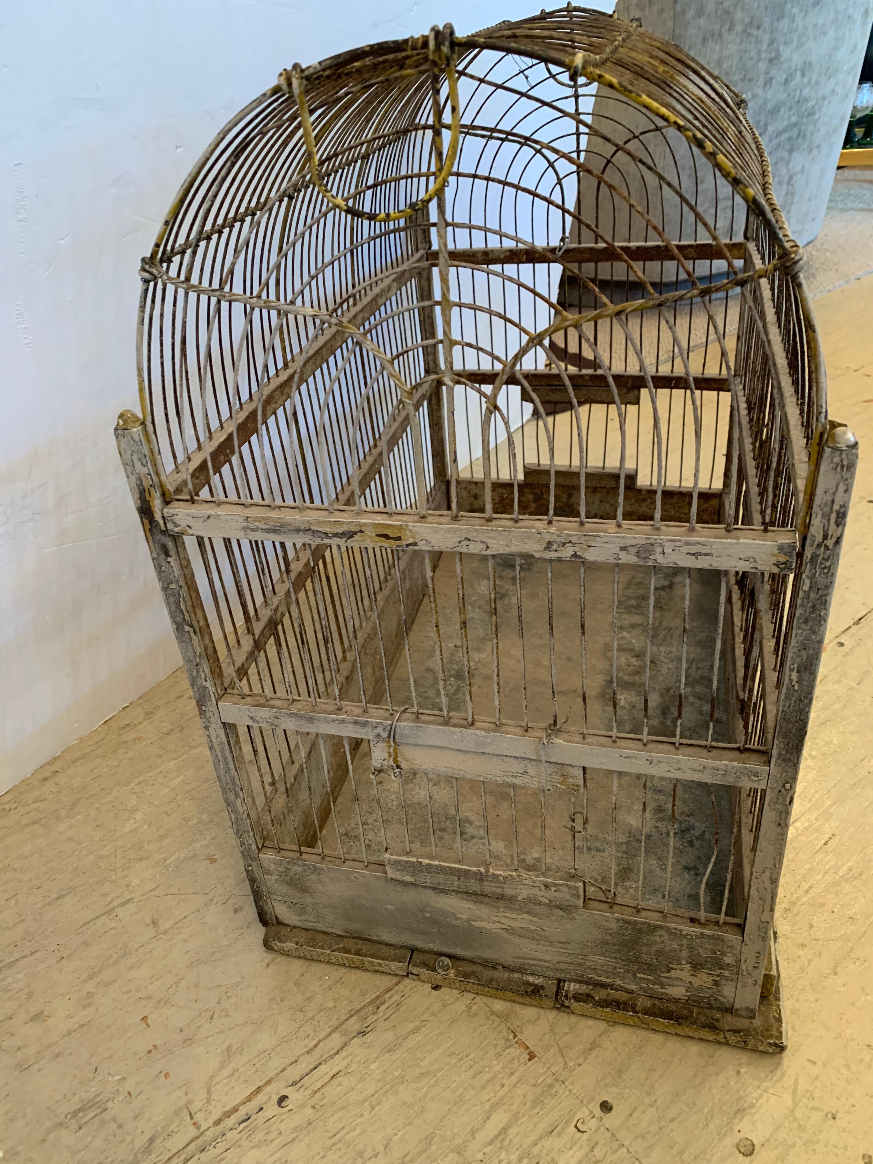 Charming metal birdcage having an arched top, steel linear cage, tin bottom, and wooden accents as well as bird perches.  There's some original chippy yellow paint that adds to the character.
 