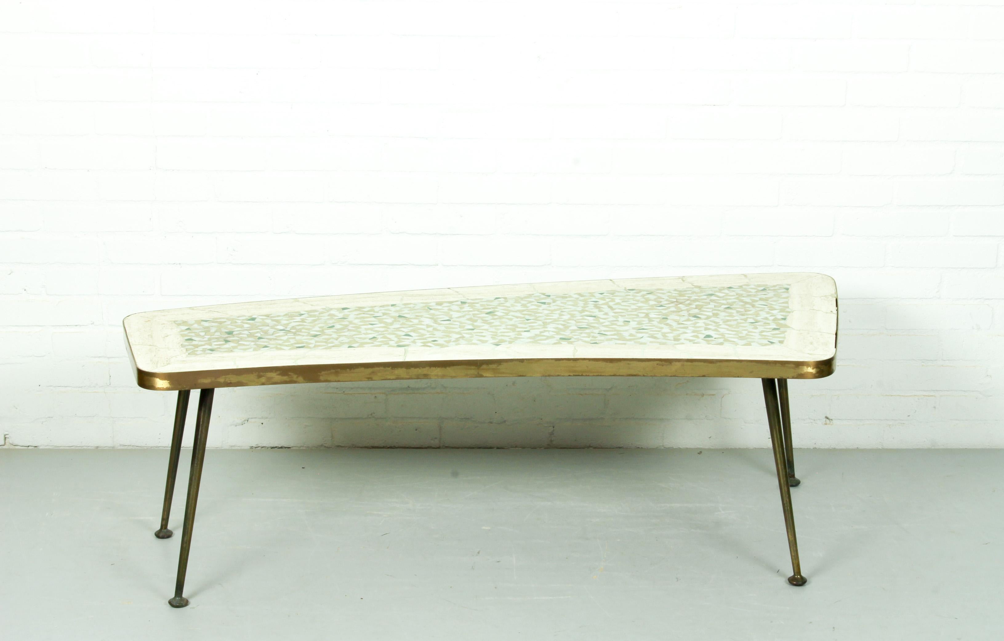 Charming midcentury organically shaped brass-leg coffee table, 1950s. The organic top surface composed of a stone mosaic in beautiful green and off-white tones interspersed with white. It has a wide border of natural and an edge of brass. The legs