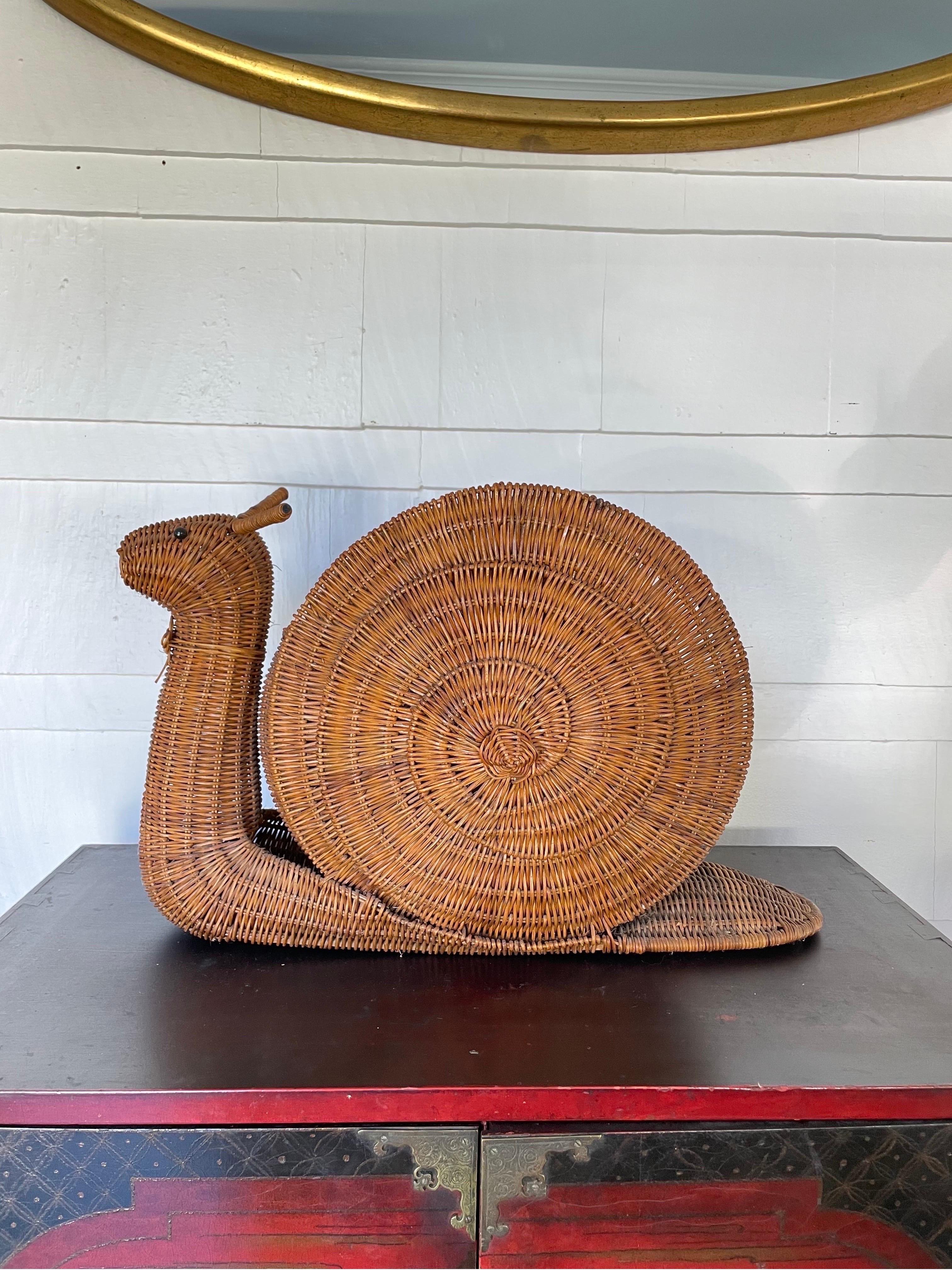 Charming mid century wicker or reed magazine stand in shape of a snail. The storage section is a snail shell in a nautilus pattern. The snail with fully equiped antennae is sporting a collar with a bow. Style meets function in a mellow, organic