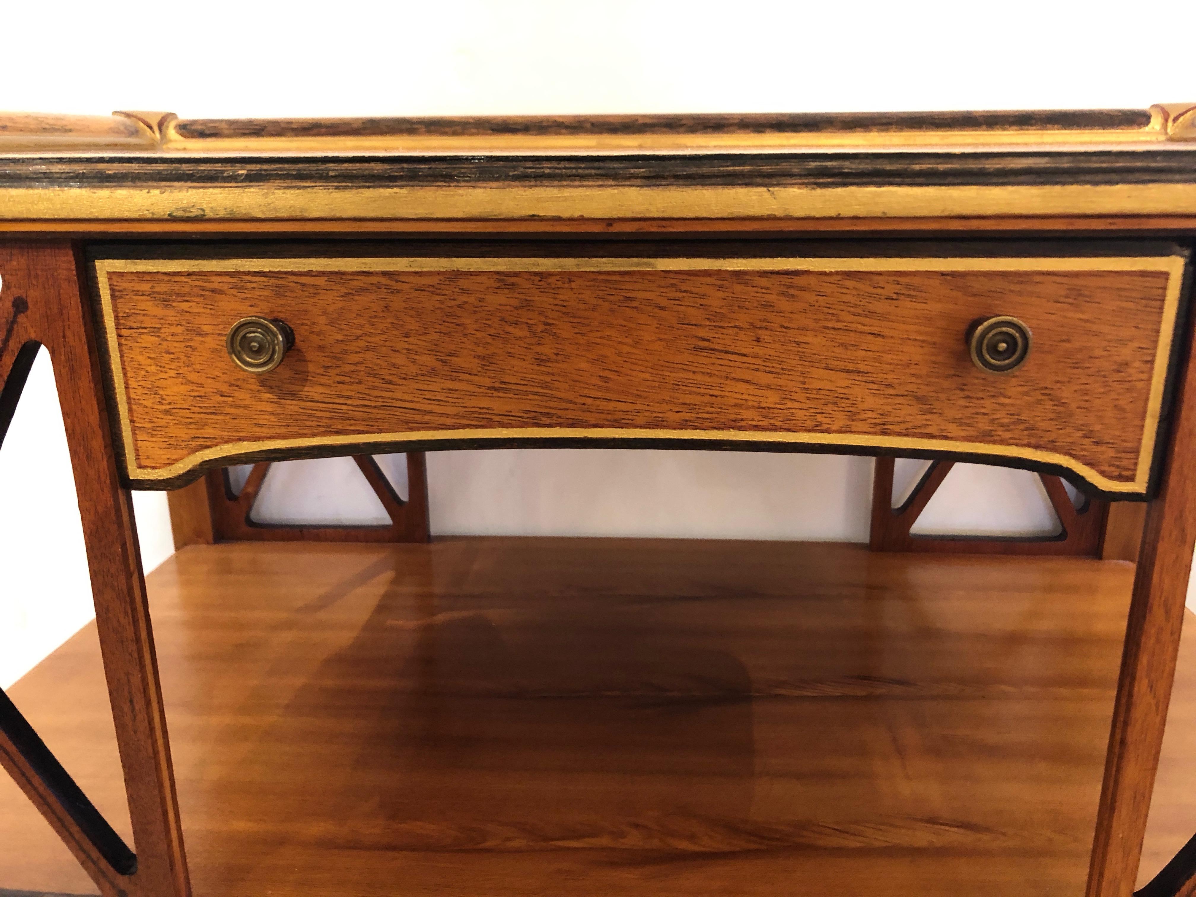 A very elegant neoclassical style side table having light brown wood offset with ebonized and painted sections as well as gold leaf. There are stunning X's on the front and back, elegant tapered legs, a single drawer, and unusual brass decorative