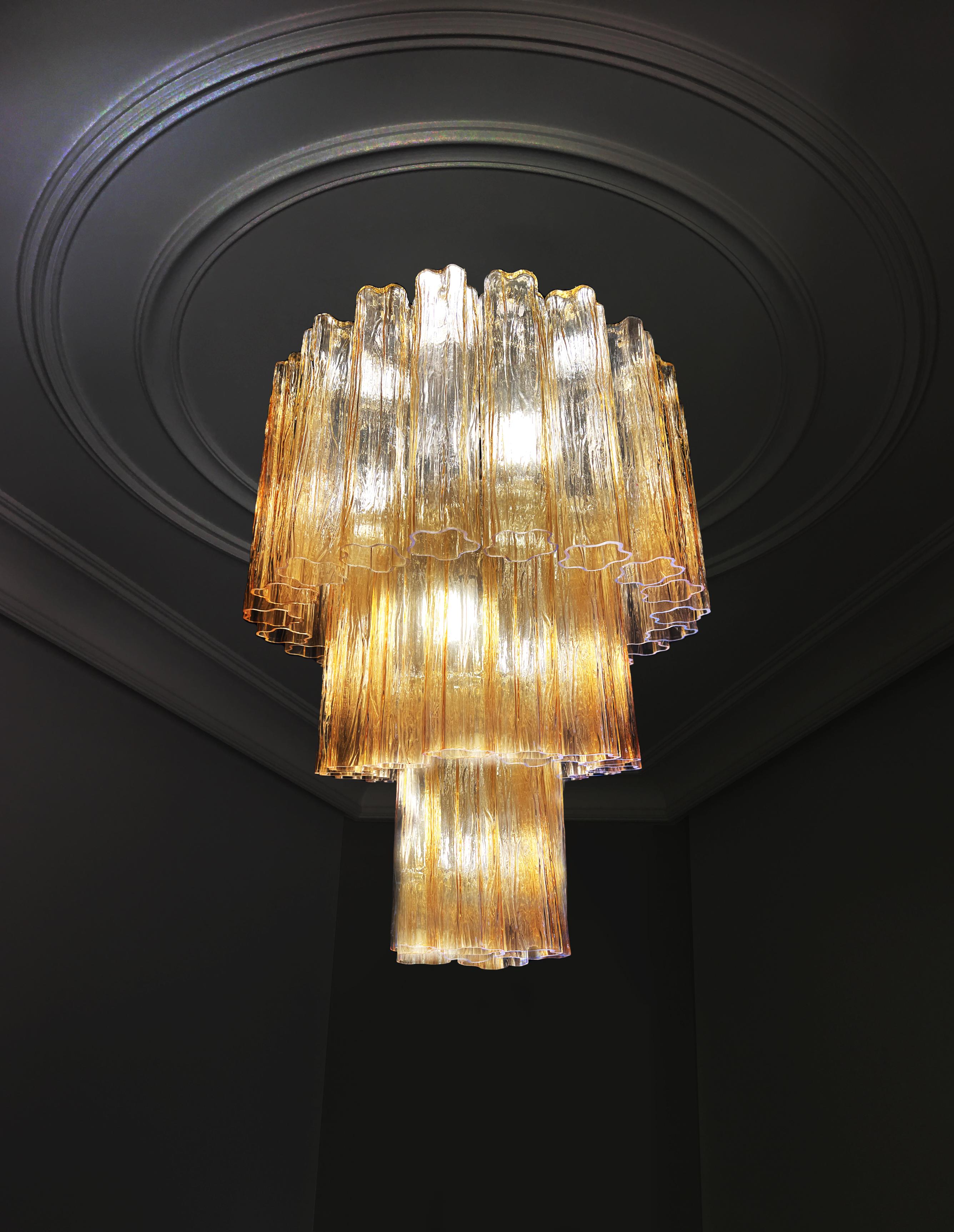 Elegant and refined pair of Murano chandeliers. The warm amber color vibrates with shades of gold, the effect is magnetic and sophisticated. The height without chain is 112 cm. It can be made to the dimensions requested by the customer.