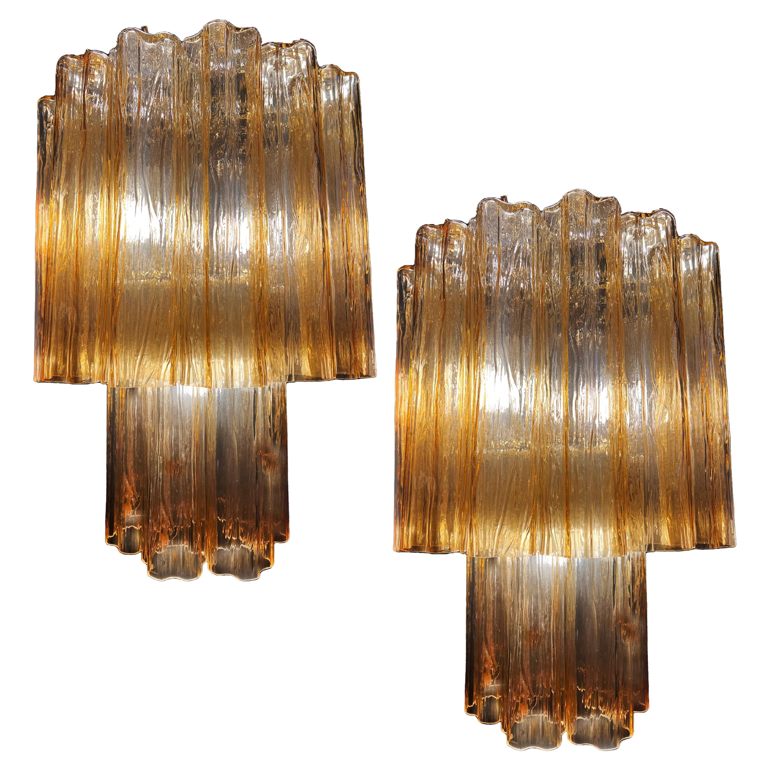 Elegant and refined pair of Murano chandeliers. The warm amber color vibrates with shades of gold, the effect is magnetic and sophisticated. The height without chain is 72 cm.