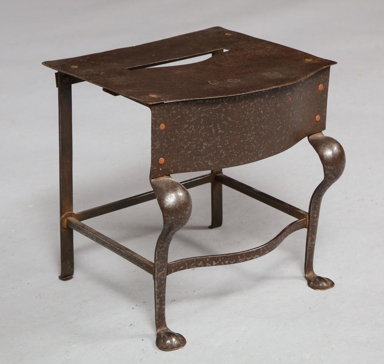 English early 19th century steel footman or trivet with bow fronted top having hand hold cutout over two cabriole front legs ending in penny feet, the rear straight legs joined by box stretchers, having nicely patinated surface.