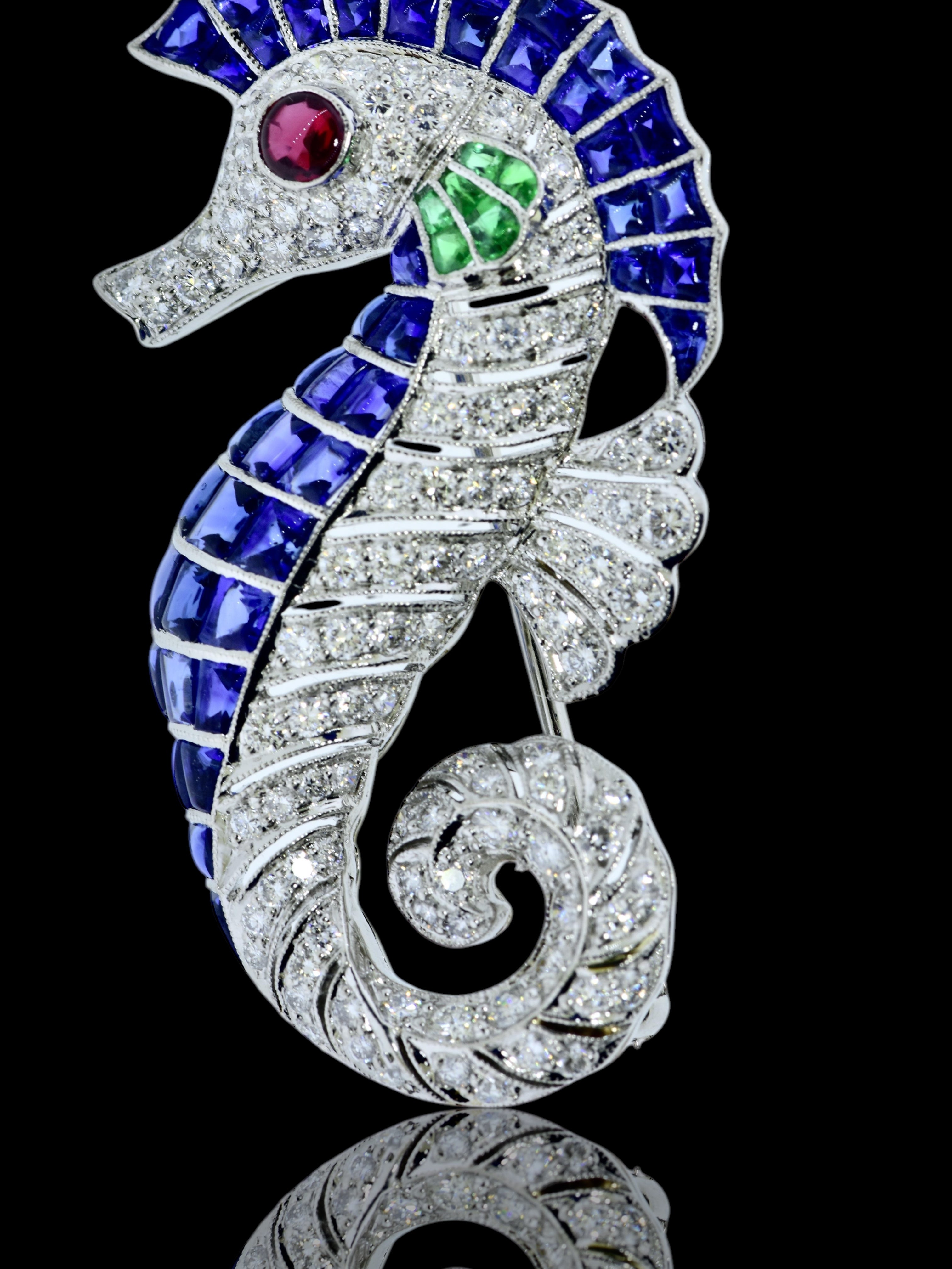 Broche en platine au motif d'hippocampe bien exécuté, sertie de saphirs, d'émeraudes, de diamants et d'un œil en rubis.  Les pierres à facettes (parfois appelées pierres en gelée) ont un pavillon à facettes et le sommet est taillé en cabochon. 