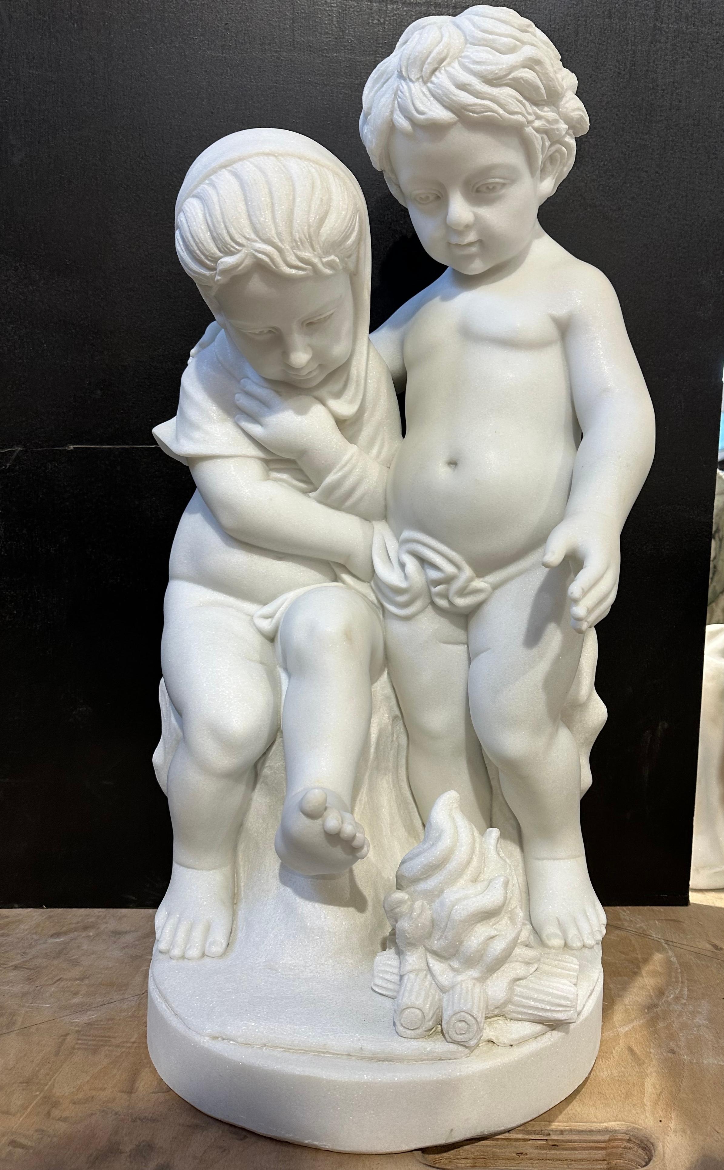 A charming white marble sculpture of two childlike putti, warming their toes on a delicately carved wood fire. 
The carving is skillful and detailed from the ruffled hair of the putti to their rounded, smooth figures and wiggling toes. 
A lovely