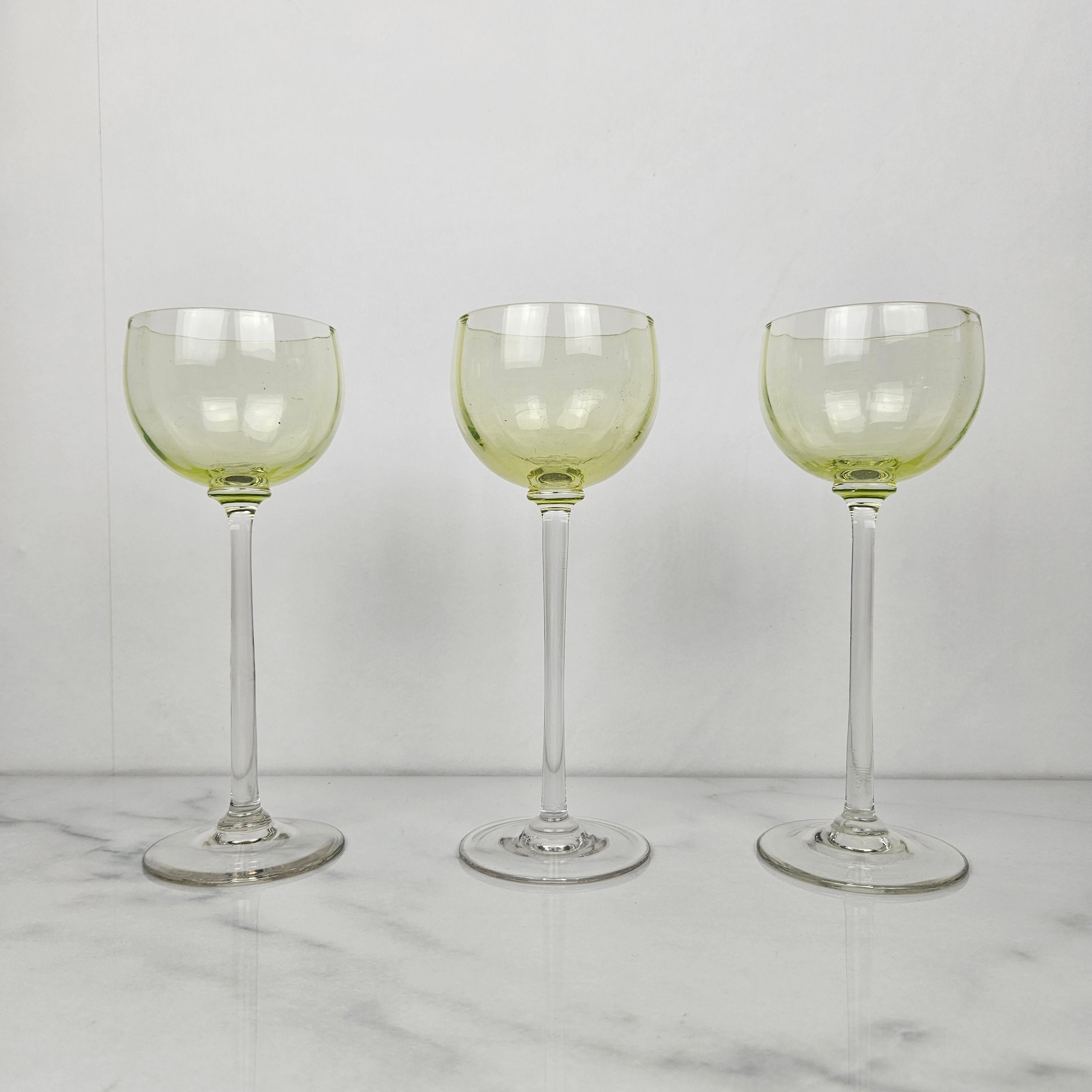 Un magnifique et rare ensemble de trois verres à vin antiques de couleur chartreuse, soufflés à la main et datant d'environ 1920. 
Chaque verre est doté d'un bol légèrement nervuré et d'une longue tige droite. Une forme élégante et allongée, à la