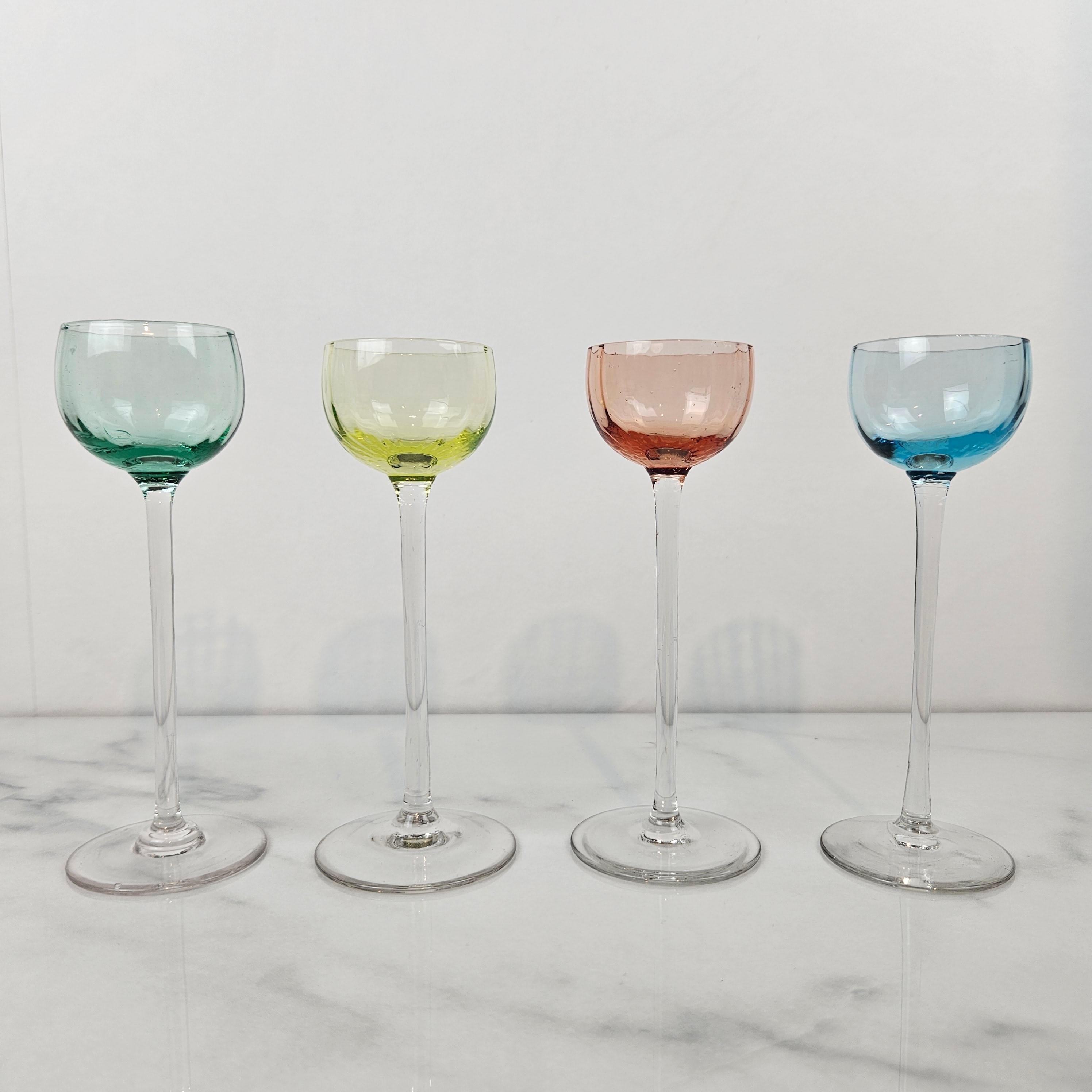 A beautiful and rare set of four antique liqueur or cordial glasses, hand-blown and dating to circa 1920. 
Each featuring a delicately handblown clear stem and subtly tinted bowl in shades of aqua green, pale yellow, rose pink, and sky blue.
An
