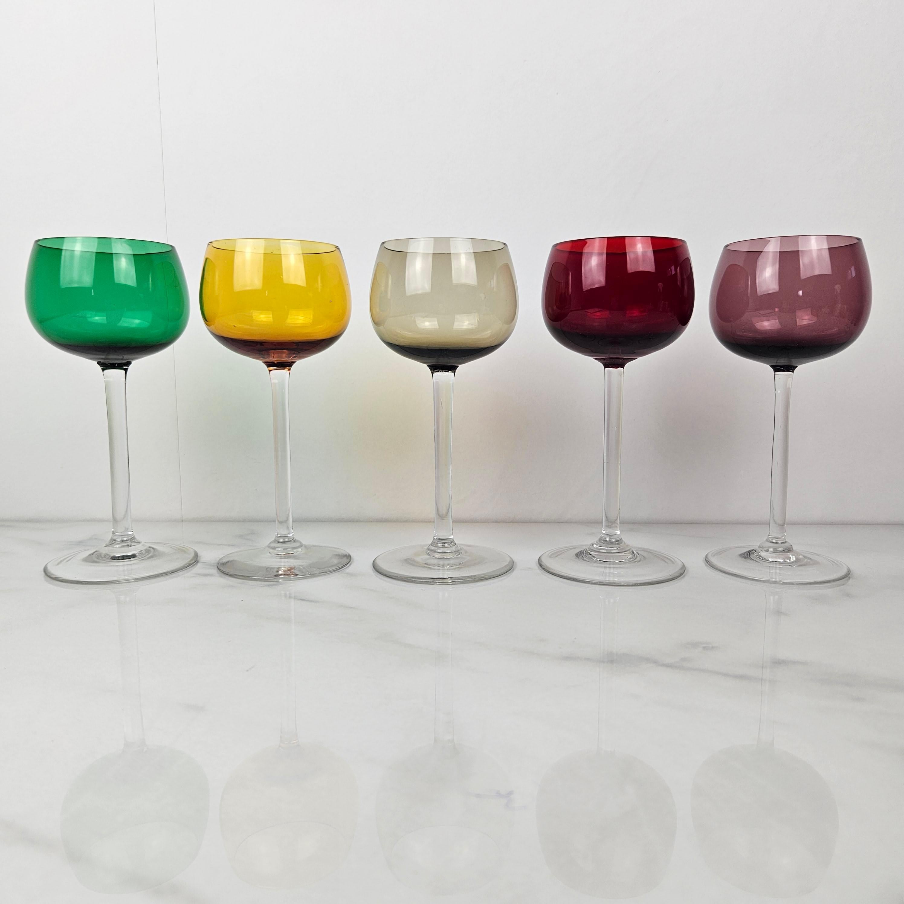 This delightful set of five antique French wine glasses offers a beautiful example of early 20th century glass craftsmanship. 
Each glass is individually hand-blown and features a vibrant bowl in a different color — green, amber yellow, smoky grey,