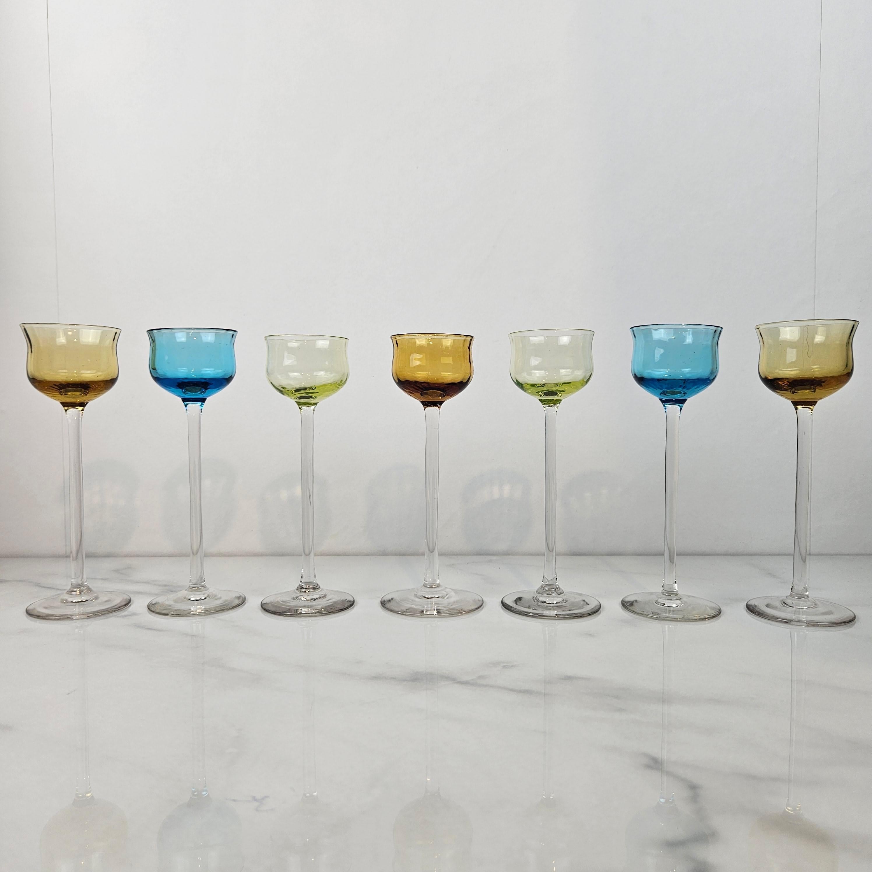 Ein schöner und seltener Satz von sieben antiken Likör- oder Schnapsgläsern, mundgeblasen und datiert auf ca. 1920. 
Jede hat einen zarten, mundgeblasenen, klaren Stiel und eine dezent getönte Schale in den Farben Bernstein, Aquablau, Champagner und