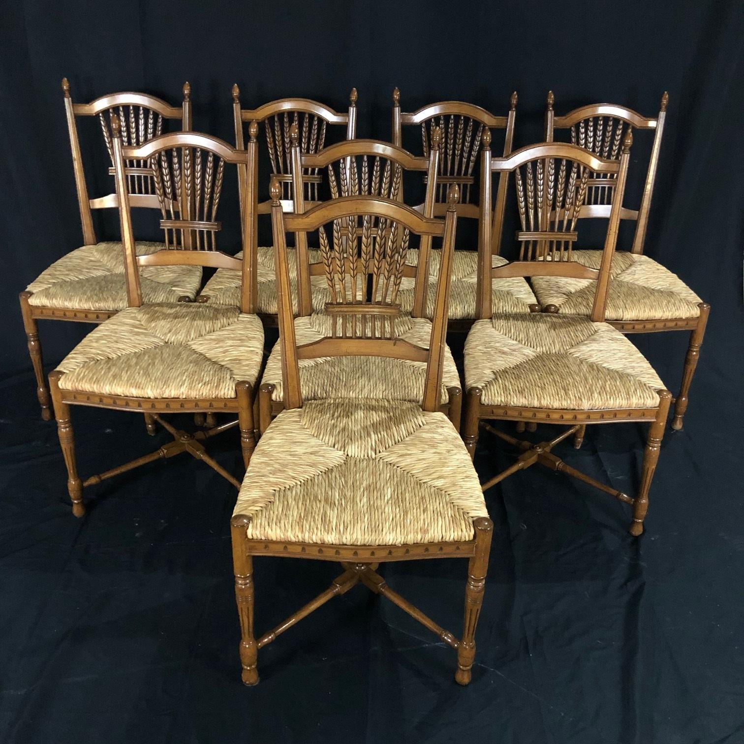A lovely and sturdy set of eight French walnut dining chairs having rush seats and wheat sheaf designed backs. The complete set showcases a carved sheaf back with turned supports. The rush seats rest on four turned legs connected to one another