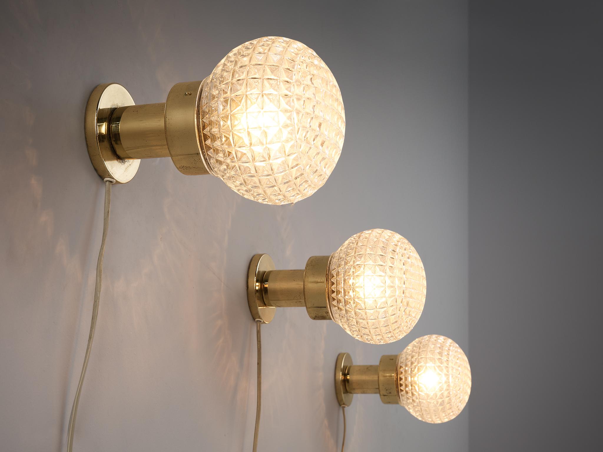 Set of three wall lights, glass, brass, metal, Europe, 1960s.

These eccentric scones or table lamps are based on a round construction. The structured glass orb is supported by a round shaped pedestal. The relief surface of the glass provides a