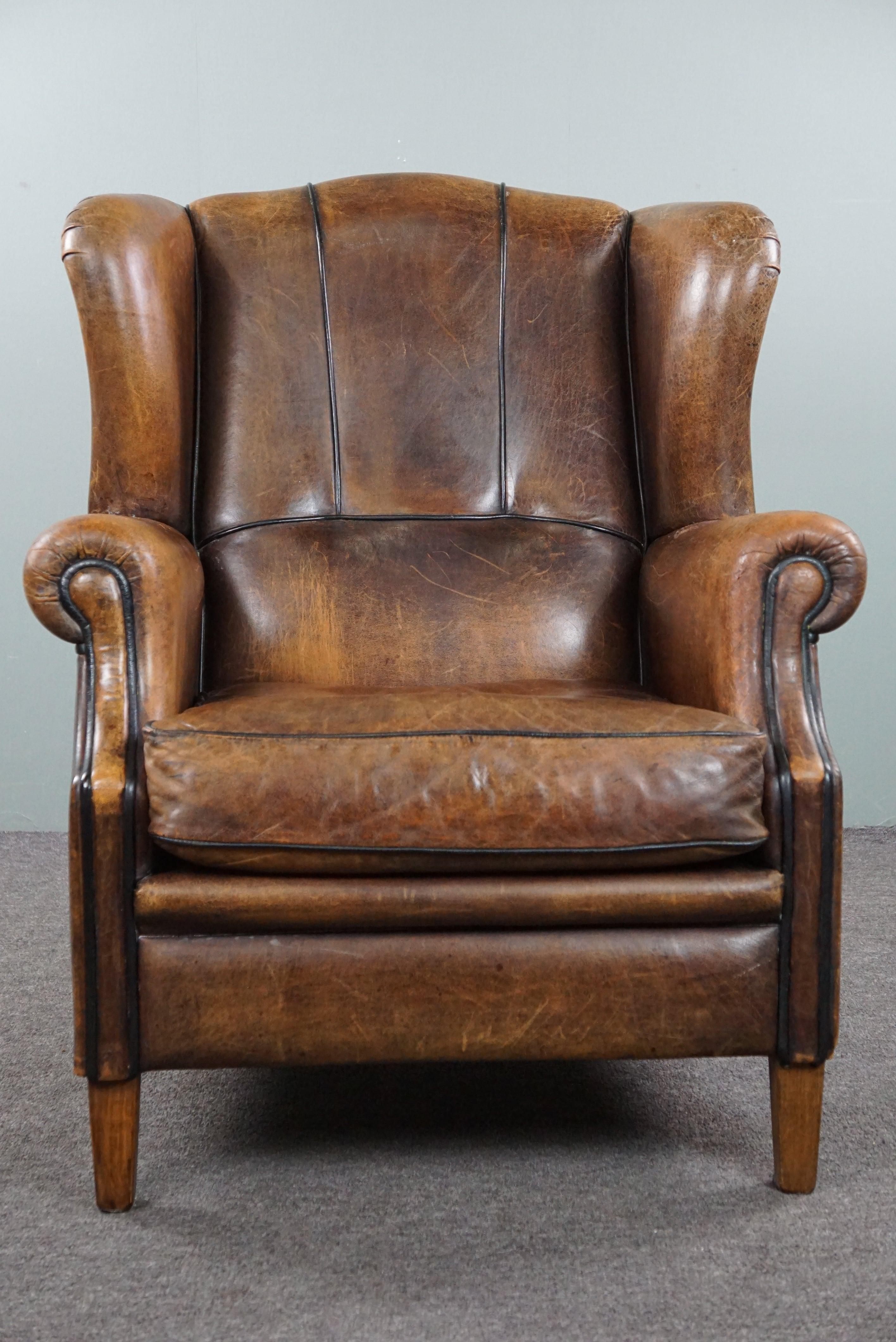 Offered is this charming positively lived-in sheepskin wingback chair finished with black piping. Through responsible use, this sheepskin wingback chair has acquired a positively lived-in appearance. The uniqueness of sheepskin leather is that signs