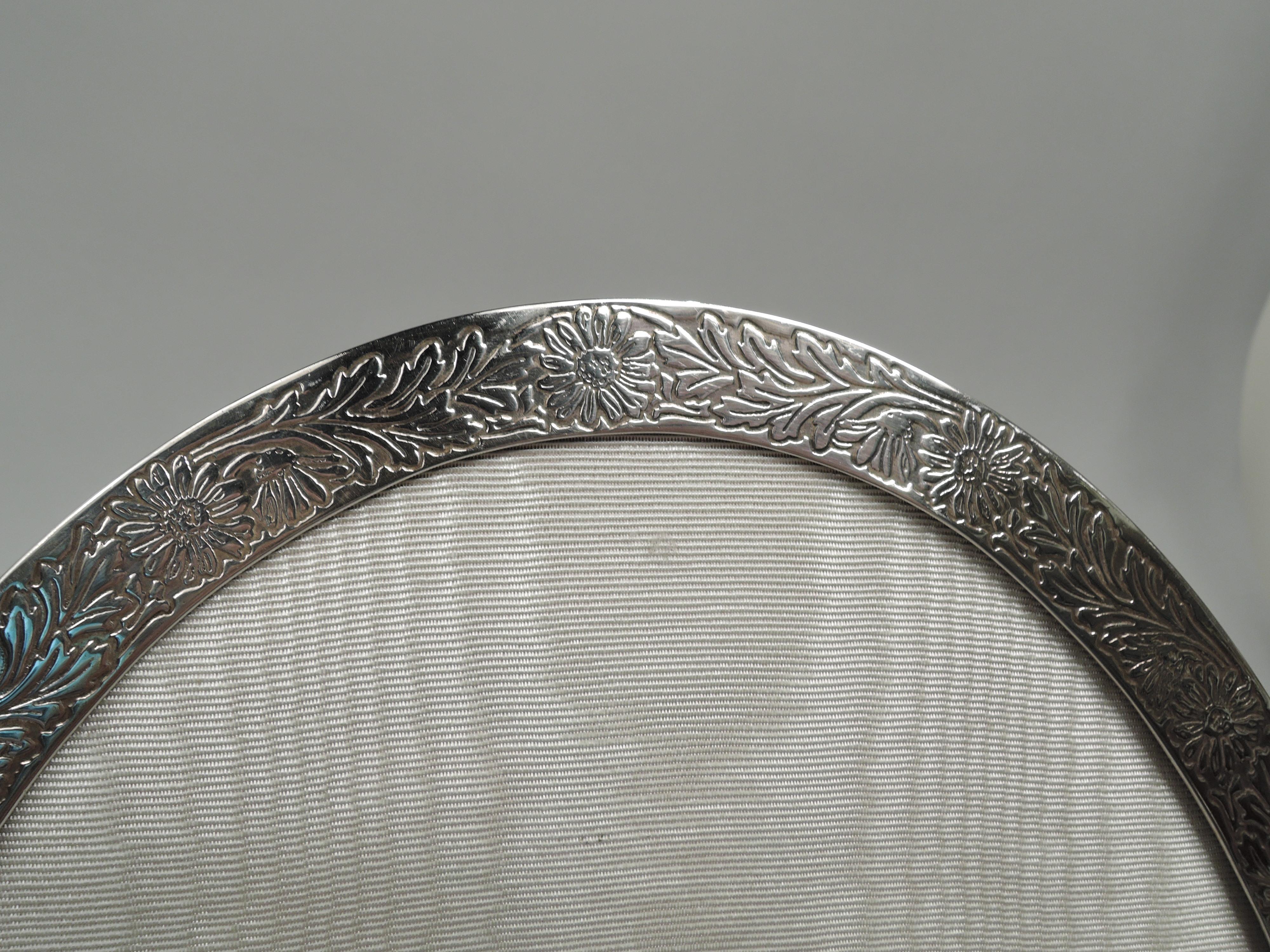 Charming Edwardian sterling silver picture frame. Made by Tiffany & Co. in New York, ca 1910. Oval window in same flat surround. On front acid-etched daisy chain with dense leaf and flower arrangement; tubular cartouche (vacant). Sides plain with