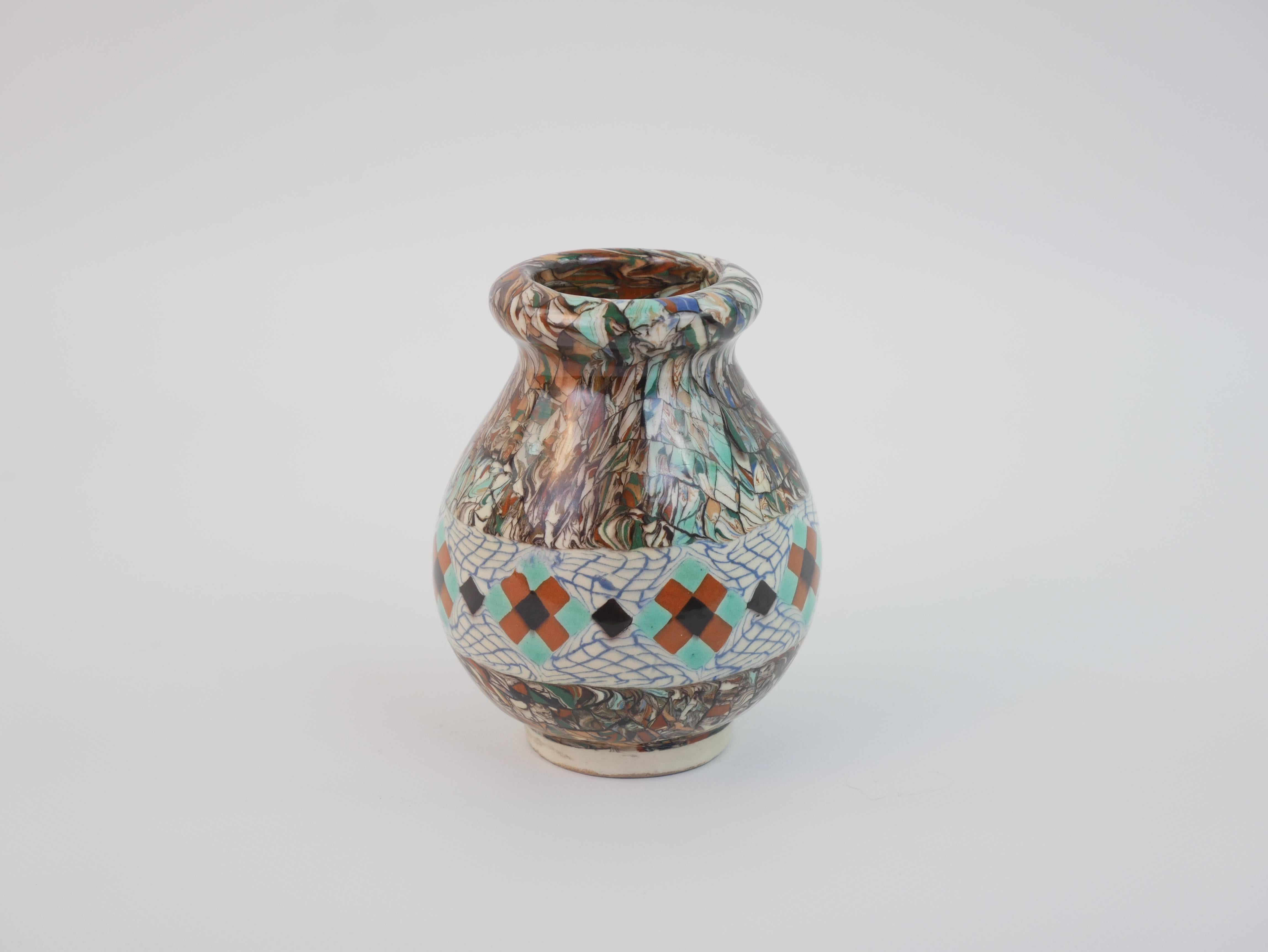 Questo piccolo vaso di Jean Gerbino, realizzato negli anni '30, esemplifica la sua iconica tecnica di mosaico in argilla. Il vaso ha una forma bulbosa ornata da motivi geometrici e floreali meticolosamente disposti nei toni della terra, del turchese