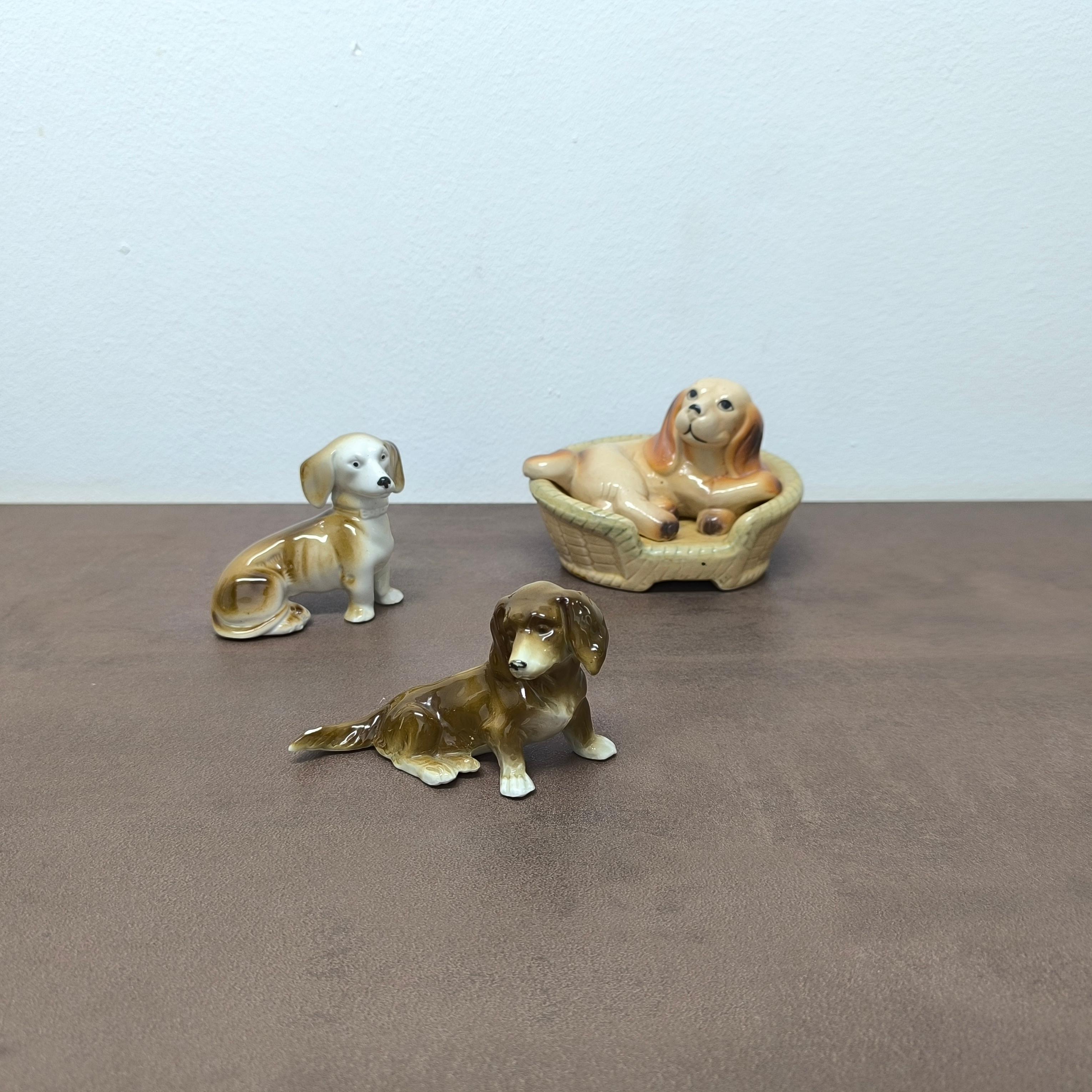 Un charmant ensemble de trois figurines de chien en céramique du milieu du siècle, chacune peinte à la main dans des tons chauds de brun et d'ivoire, avec des expressions et des poses réalistes. 
Ce trio sculptural comprend :
- Un chiot couché niché