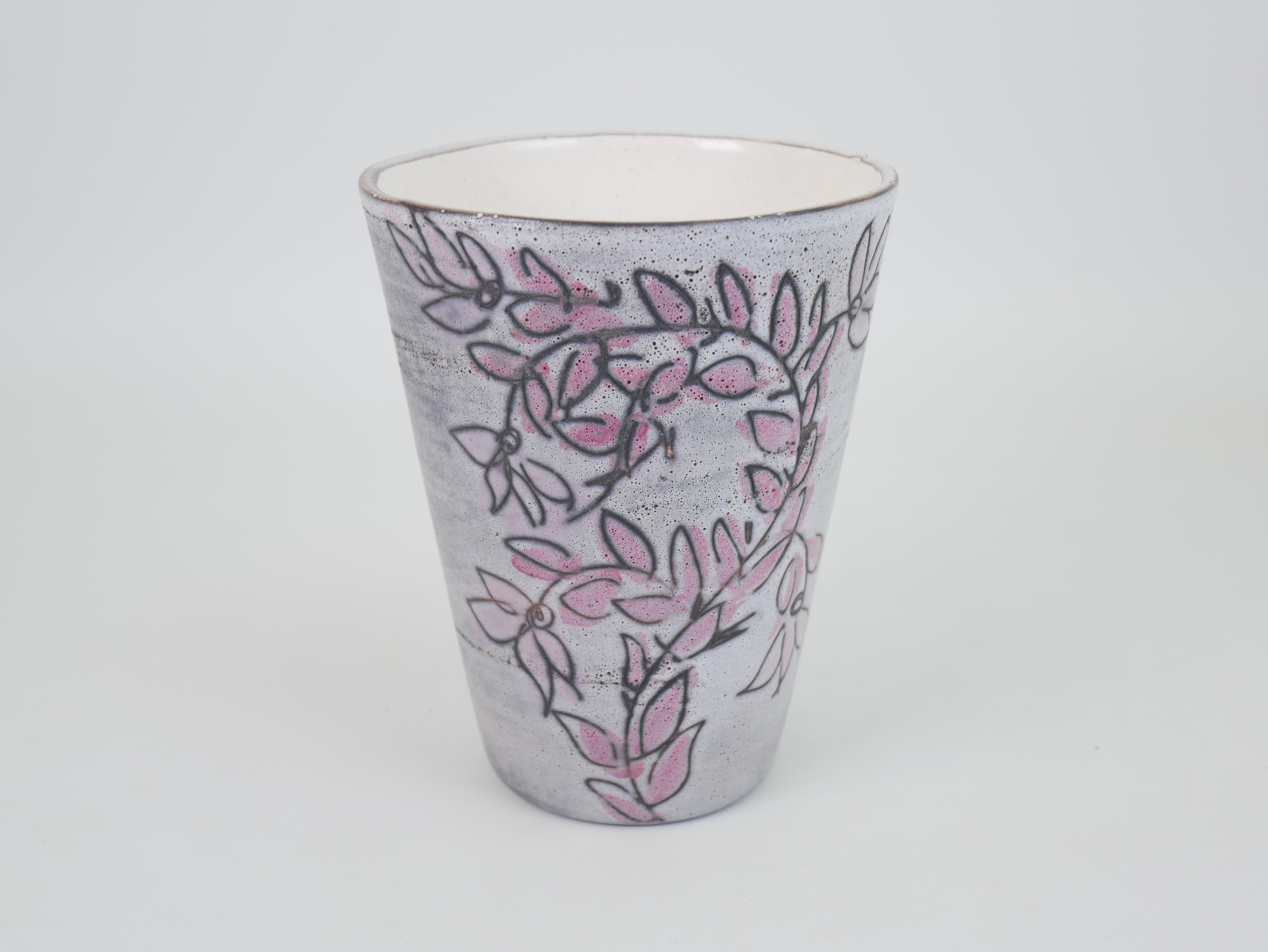 Il s'agit d'un vase en céramique de 15 cm de haut, signé sur la base, réalisé par le célèbre artiste français Roger Capron. Le vase présente un fond gris doux et mat avec de délicats motifs floraux roses et noirs qui s'enroulent gracieusement autour