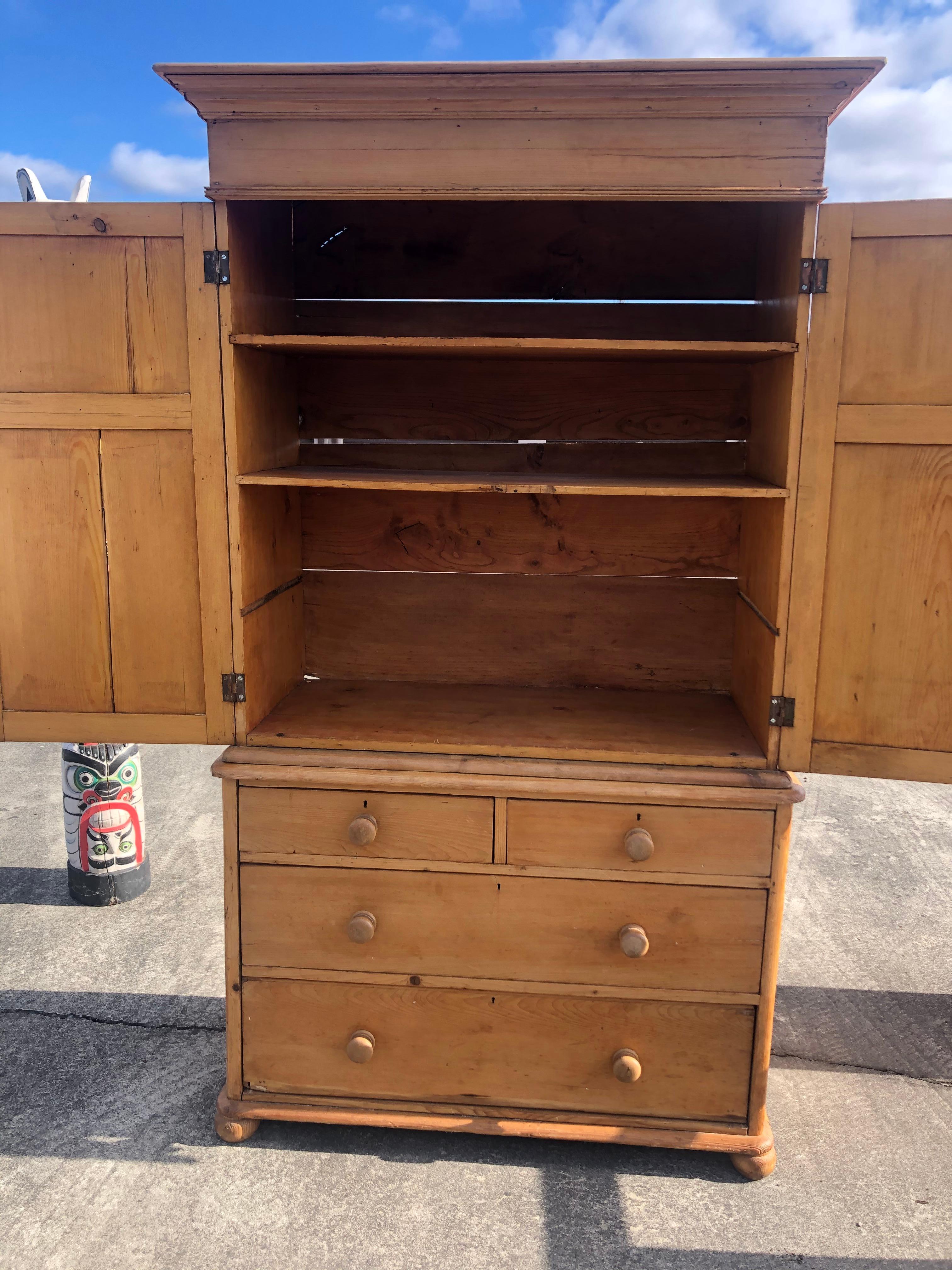 A rustic antique natural pine cabinet wardrobe in two pieces; top has panel doors that open to roomy storage, once used to house a television. There are two shelves currently. Bottom has 4 dovetailed drawers, 2 large with 2 smaller on top. The