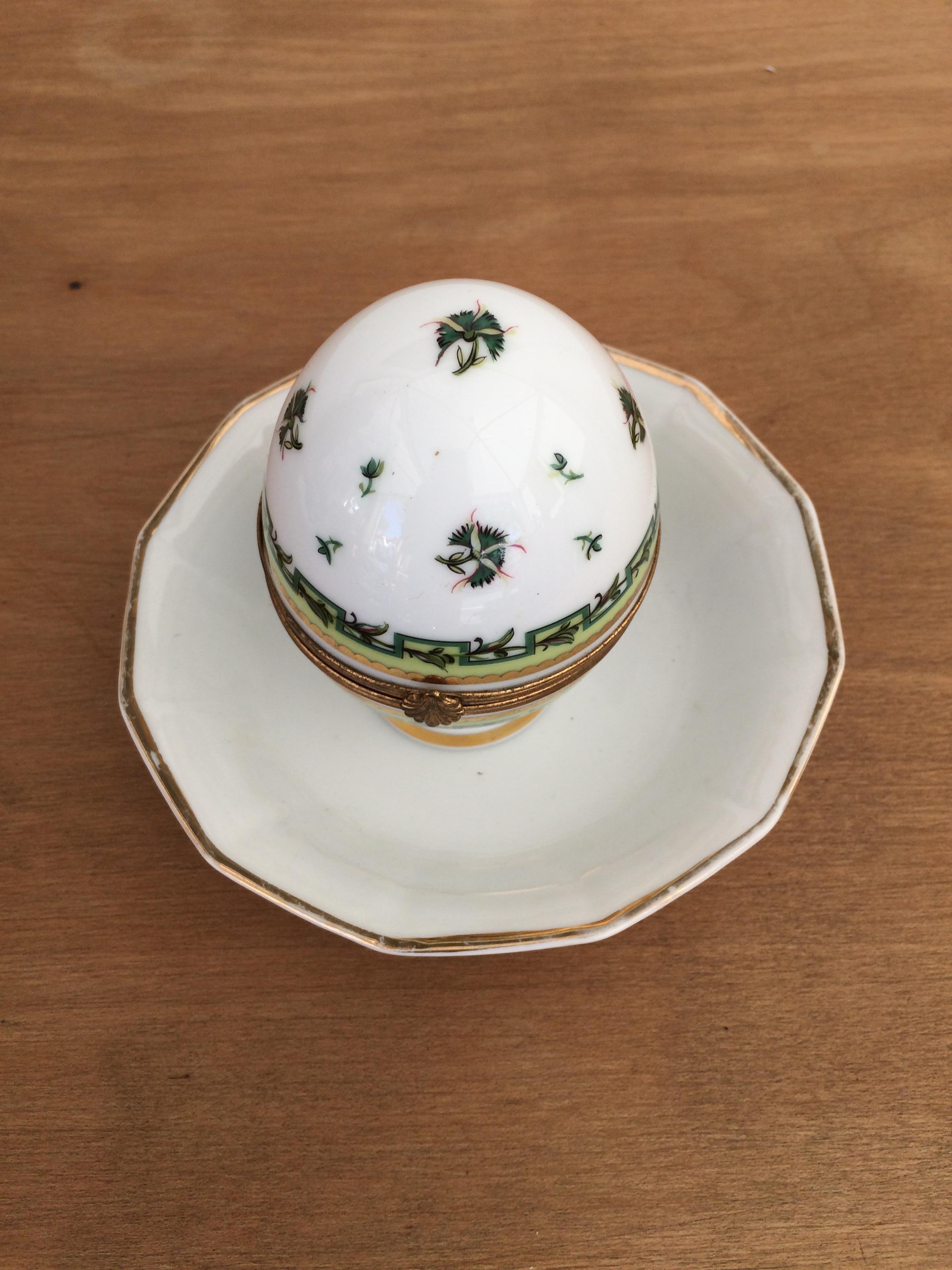 This French limoges porcelain trinket box is a delicate egg shape with a floral decorated closure. It is charmingly hand painted with on a solid white background. The interior hinges opens to reveal the word Bougainville which is also hand painted.