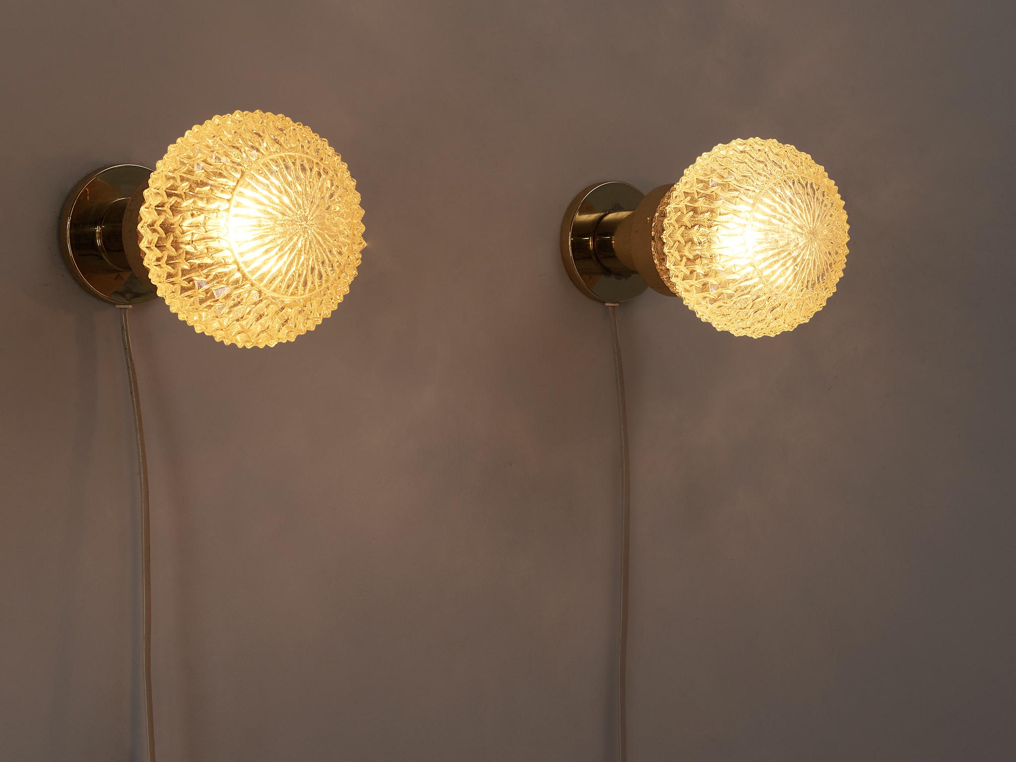 Wall lights, glass, brass, metal, Czech Republic, 1960s.

These eccentric scones or table lamps are based on a round construction. The structured glass orb with an ocher tone is supported by a round shaped pedestal. The relief surface of the glass