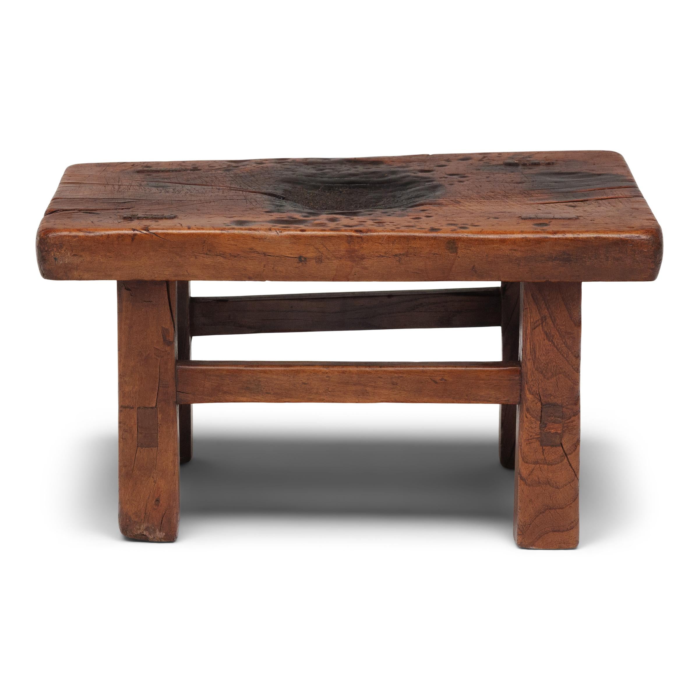 Dieser schlichte Hocker aus der Mitte des 19. Jahrhunderts vereint die Einfachheit der Form mit der unnachahmlichen Schönheit einer alten Patina. Der niedrige Hocker ist aus Ulmenholz mit traditionellen Schlitz- und Zapfenverbindungen gefertigt und