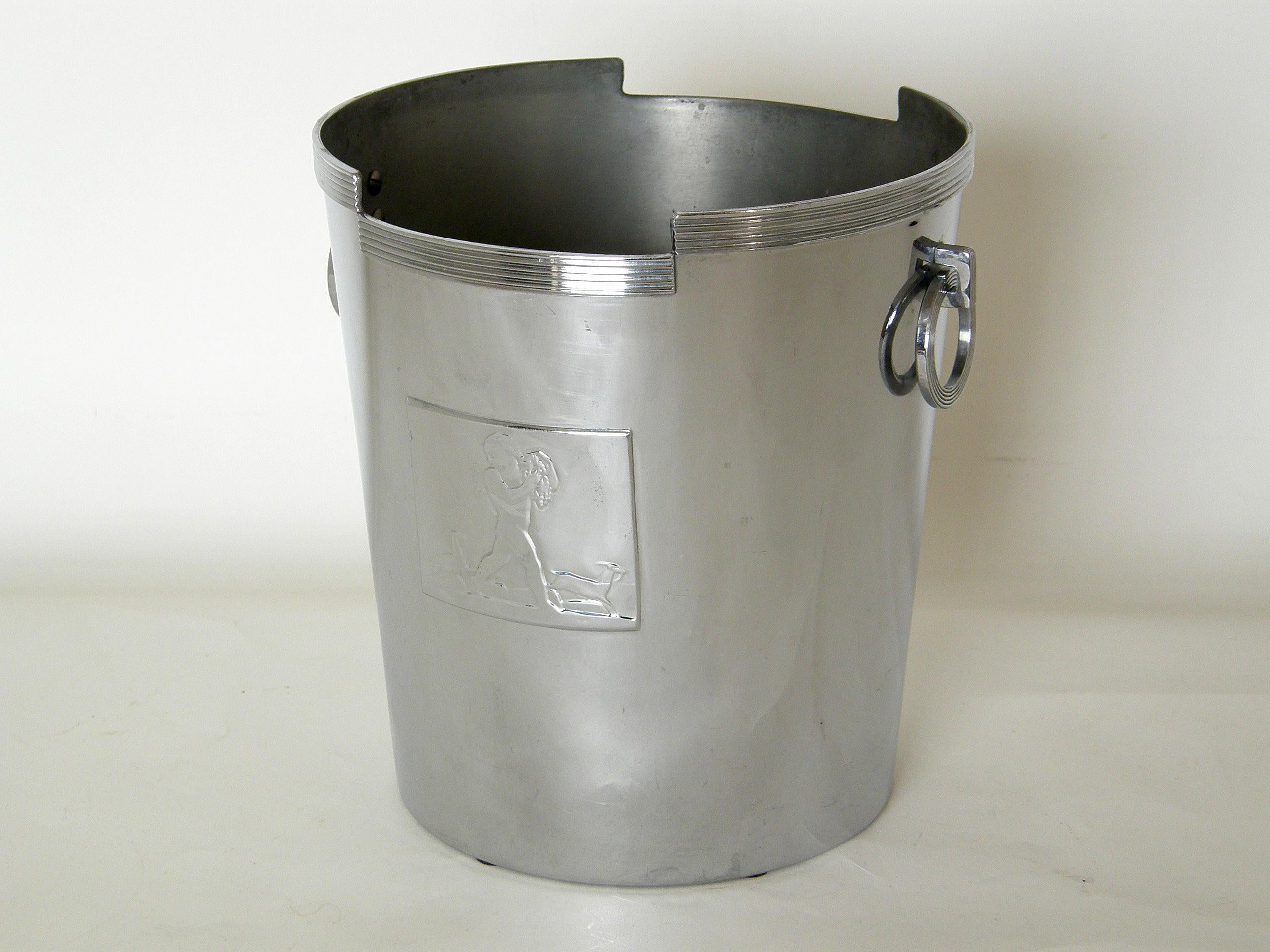 This chrome-plated champagne bucket has a Classic Art Deco style. The top edge is stepped and trimmed with a ribbed band; the front is adorned with a decorative plaque depicting Bacchus and two deer; and the ribbed ring handles hang from the sides.
