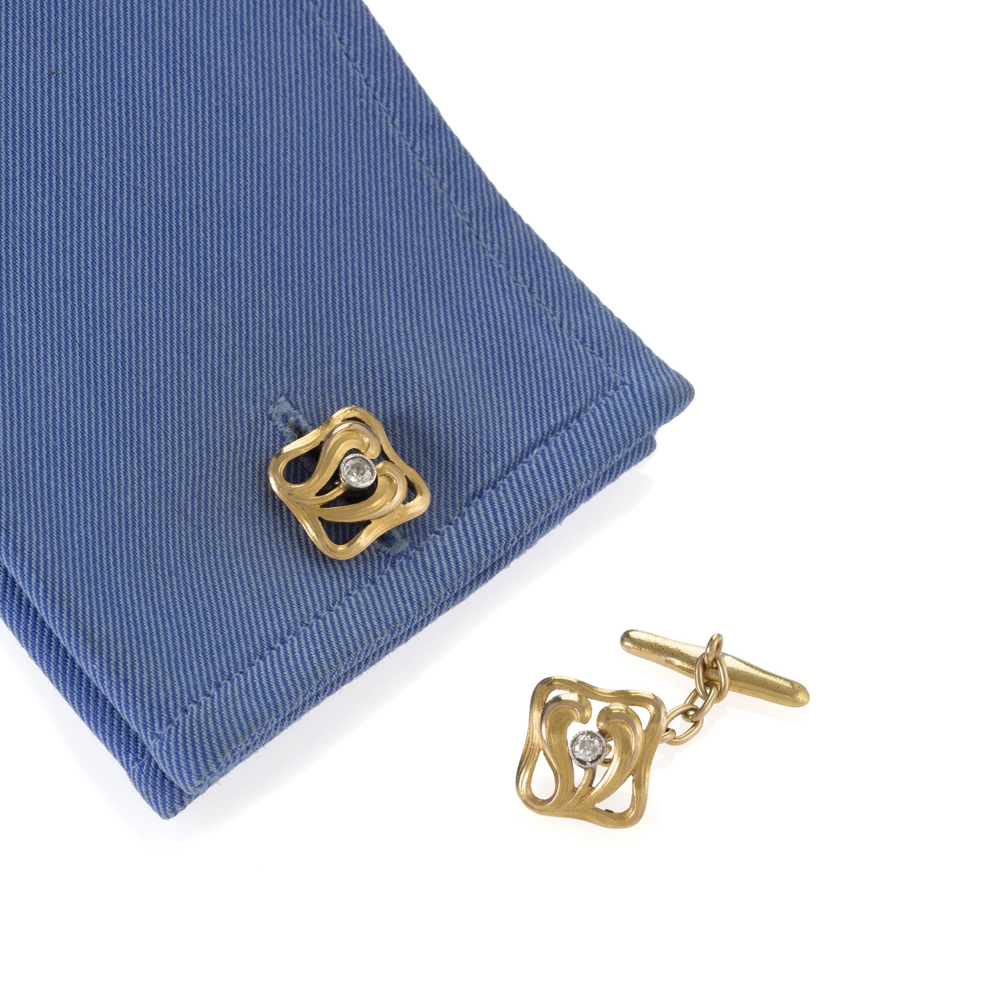 These French gold cuff links with diamond accents date from the Art Nouveau period. Each cuff link is designed as a chased and engraved sinuous vine enclosing two fronds, highlighted by a diamond bezel-set in platinum, and joined by trace link chain