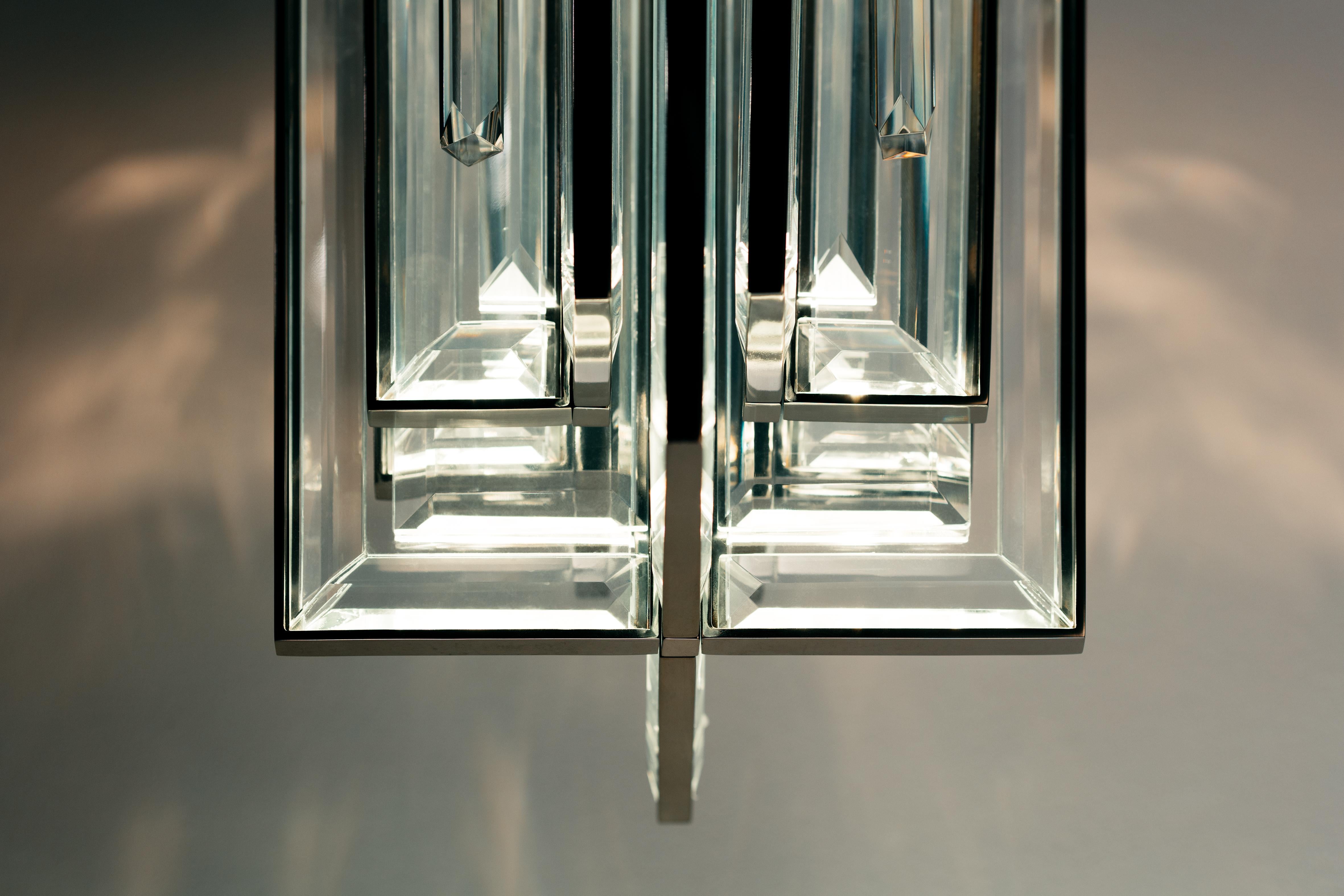 A prism of beveled glass blades and glass rods, surrounded by clear crystal and set in a softly stepped metal housing. The interlocking design fixes elegantly to a wall plate to create an atmospheric volume of light, easily adjusted to create mood