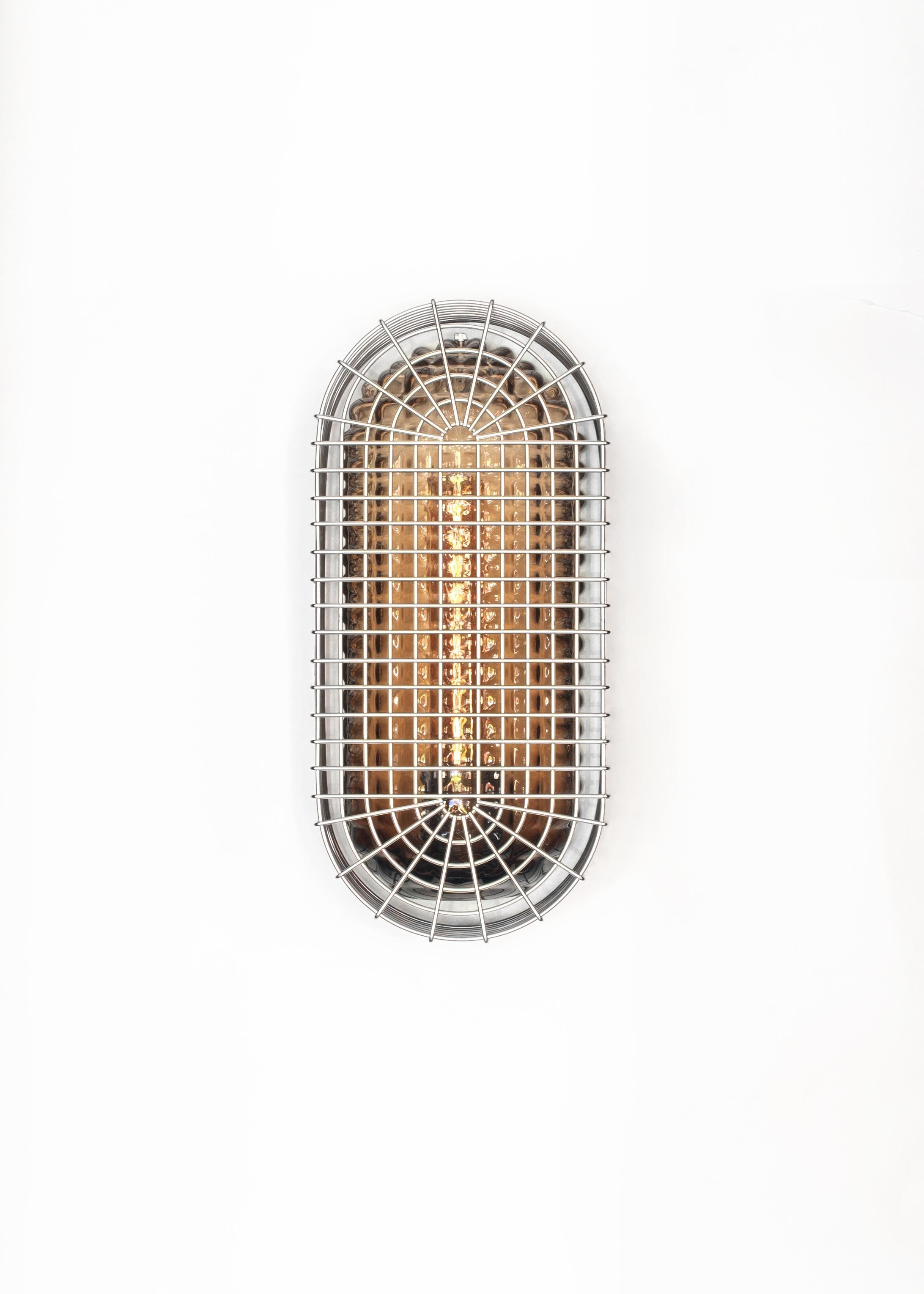 With restraint comes anticipated pleasure. Such is the philosophy behind our Chastity Sconces. Rippled glass lies underneath a cage of stainless steel to juxtapose sinuousness and rigidity. The glow of the underlying light accentuates the layering