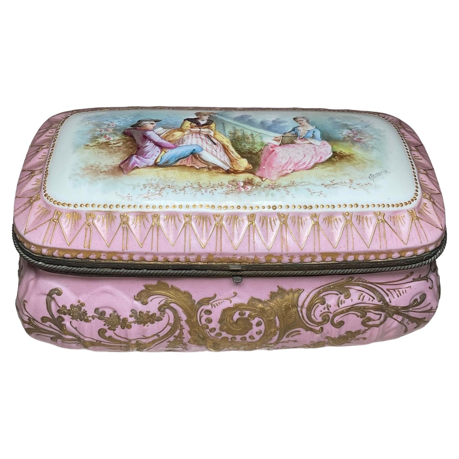 This is a Chateau de Tuileries hand painted porcelain rectangular casket box. It depicts a pastoral scene of a young couple and their chaperone over it’s hinged lid. The scene is framed by a pattern of gilt pink arrow tips. The side panels of the