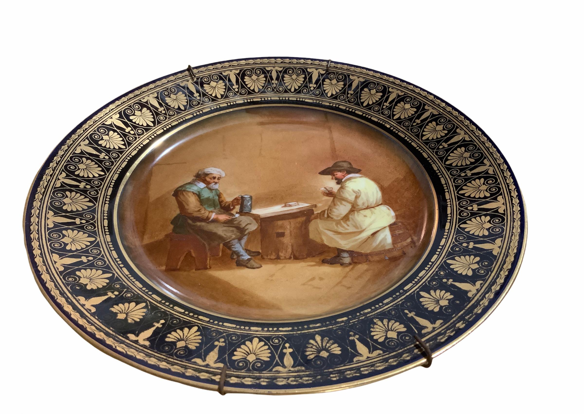 This a Chateau de Tuileries hand painted porcelain cabinet plate. It depicts a scene of a pair of country men that are sitting, one in a wood bench and the other one in a barrel while they are playing cards in a tavern. There is also a small rustic