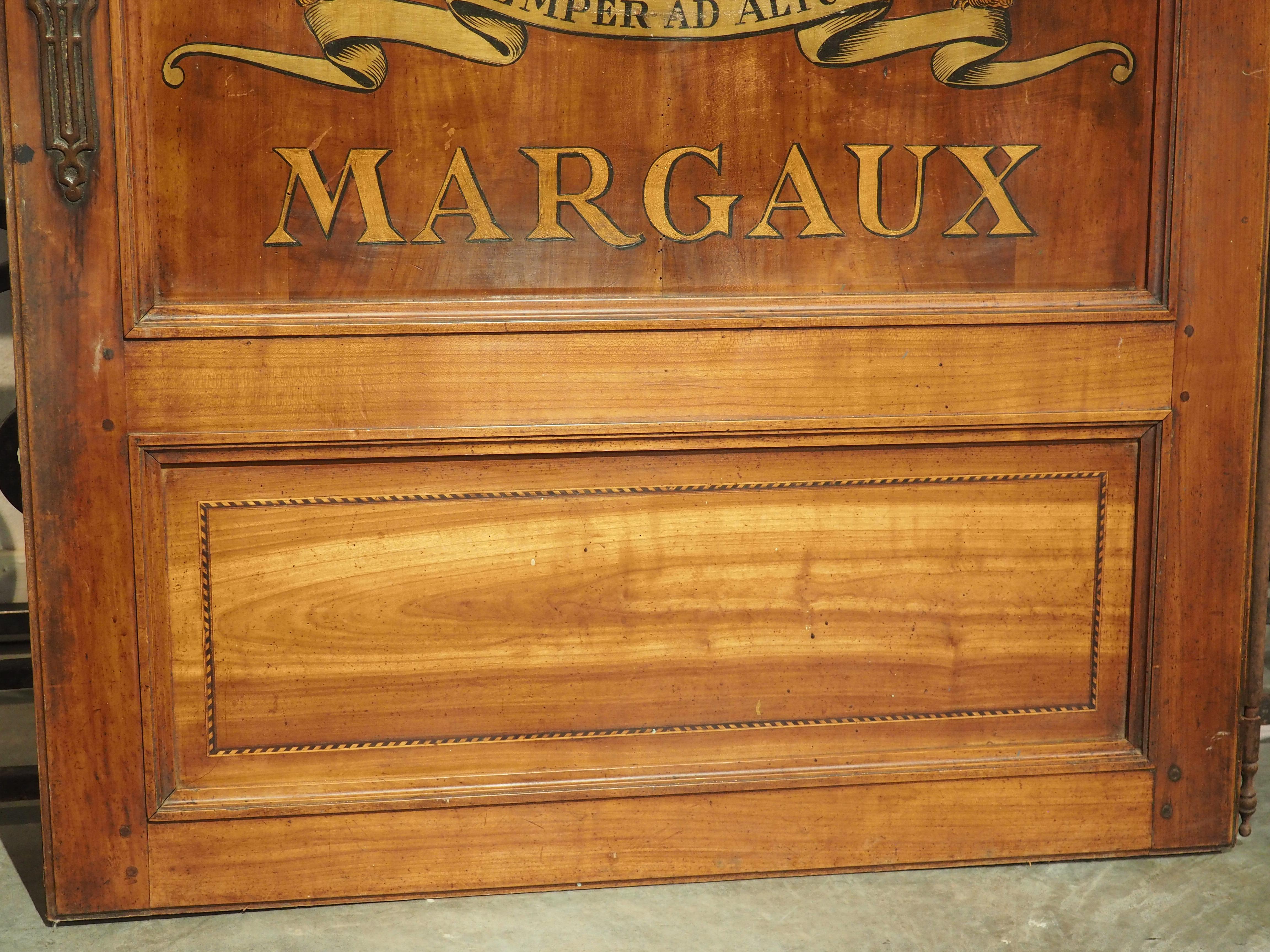 Originally part of a large antique French cabinet (Buffet Deux Corps), this cherrywood door has a stylized logo of a Medoc region vineyard painted on the frontage. The main panel of the rectangular door has a shaped upper molding with a pair of