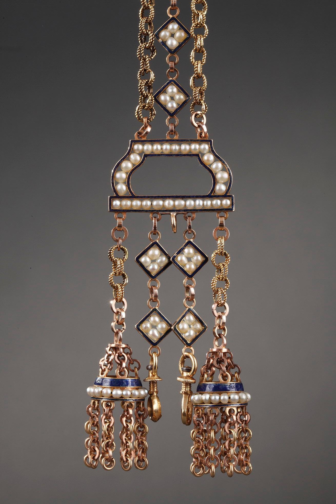 Chatelaine composed of gold overlaid with royal blue enamel. Two gold link chains flank a central chain whose diamond-shaped links are each decorated with four pearls. These three chains are attached to an enameled half circle that is embellished