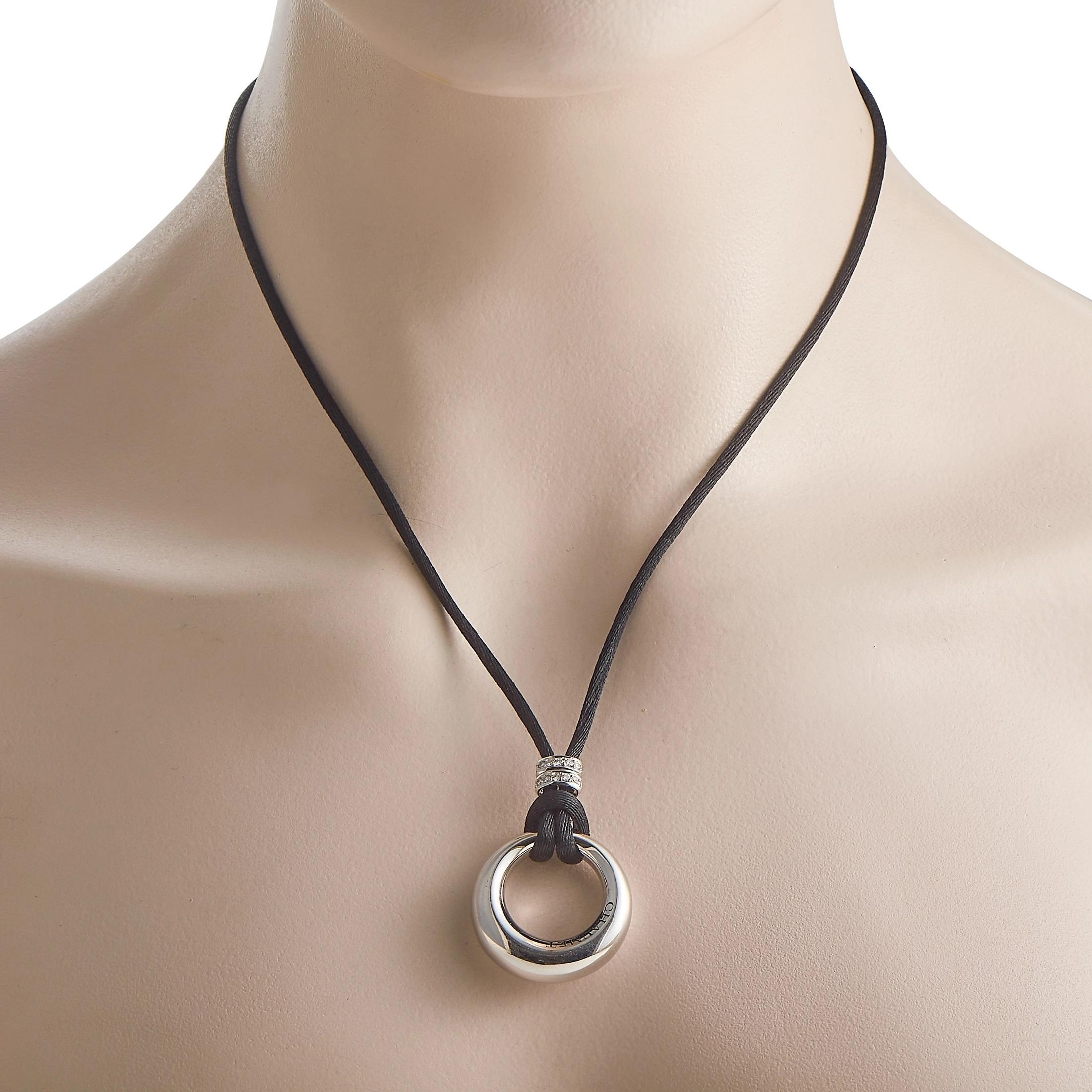 A sleek, circular 18K White Gold pendant measuring 1.5” long and 1.15” wide makes this Chaumet necklace a minimalist piece with a unique sense of style. Accented by glittering diamond charms, its suspended upon a contemporary 30” long black cord. 
