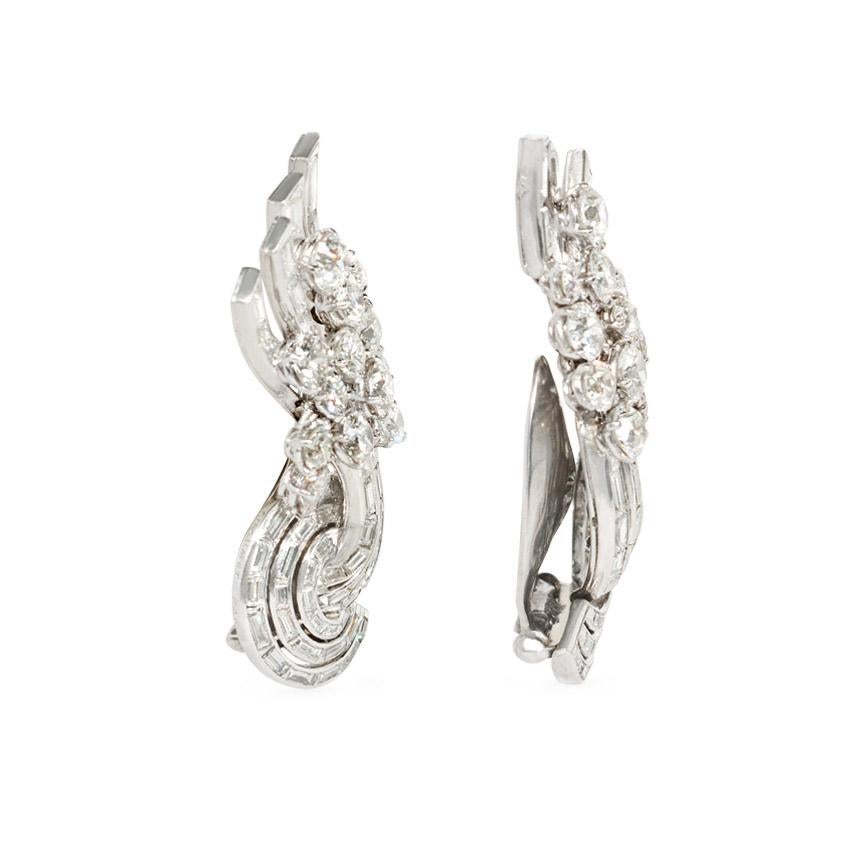 A pair of Art Deco diamond up-the-ear earrings of scrolled design with concentric circular ornaments and diamond fan-shaped tails comprised of rounds and baguettes, in platinum; also wearable as dress clips. Chaumet, Paris.  Atw. 15.00 cts.  In