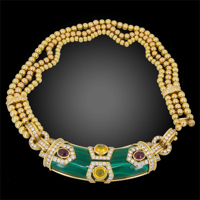 A collar necklace, designed with three rows of 18kt gold beads, centered a polished malachite plaque, accented with oval cabochon rubies, yellow sapphires, and round diamonds,  signed Chaumet, Paris, with French assay and maker’s marks.
length