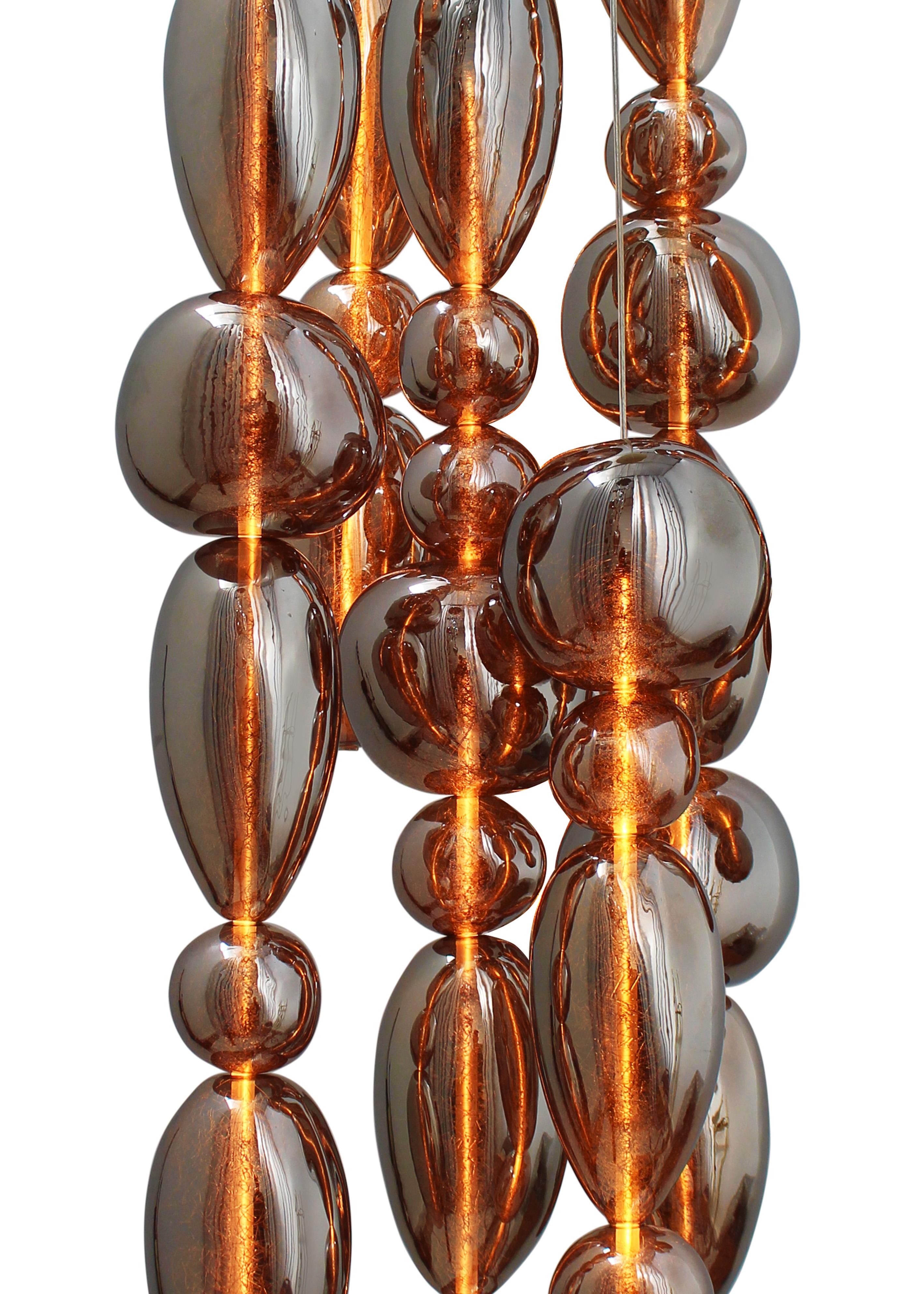 Pendentifs en verre transparent soufflé à la bouche. 
13 colonnes en verre sur un baldaquin rectangulaire de 150 x 10 cm en laiton brossé.

La collection Chavana présente des verres inspirés de galets empilés le long d'un tube LED de 17W,