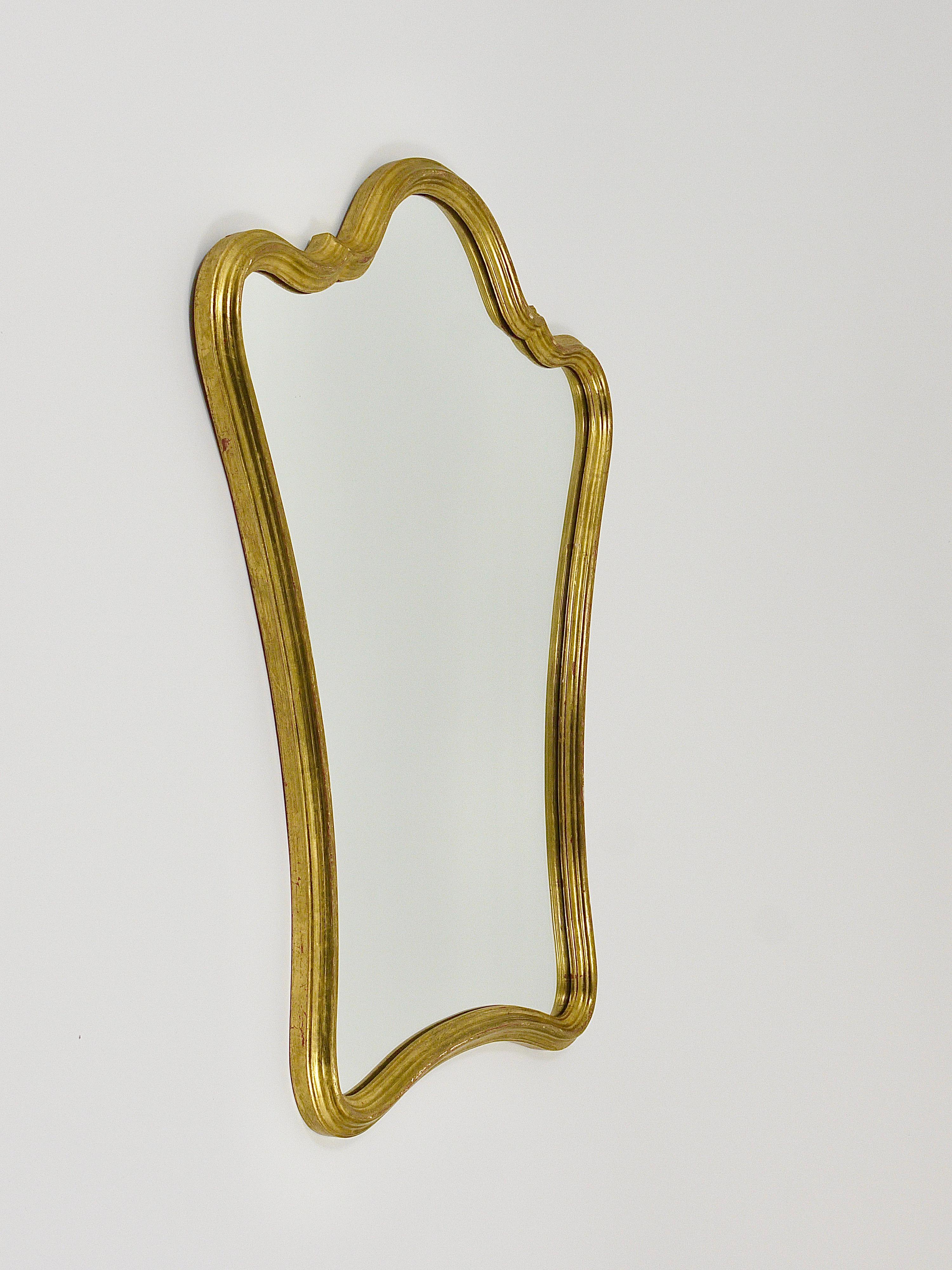 A charming Italian Mid-Century modernist wall mirror manufactured in the 1950s by Chelini C. N. Firenze in Florence, Tuscany, Italy. It is handmade from wood with a gold leaf finish. The frame features a beautifully curved shape and is in good