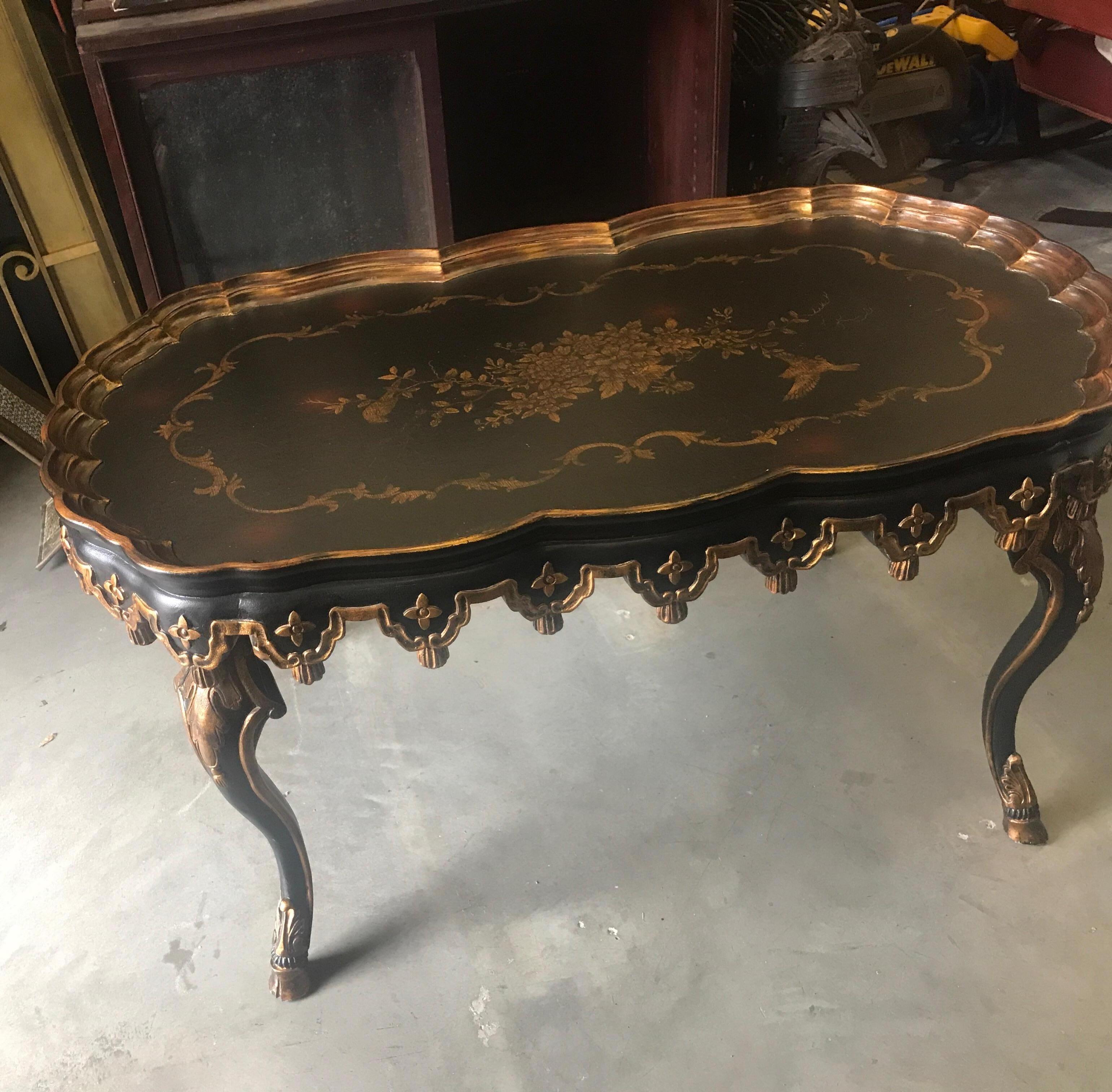 High style gilt decorated coffee table with crackled black background. The scalloped tray style edge with nicely detailed aprin resting on four curvaceous legs.