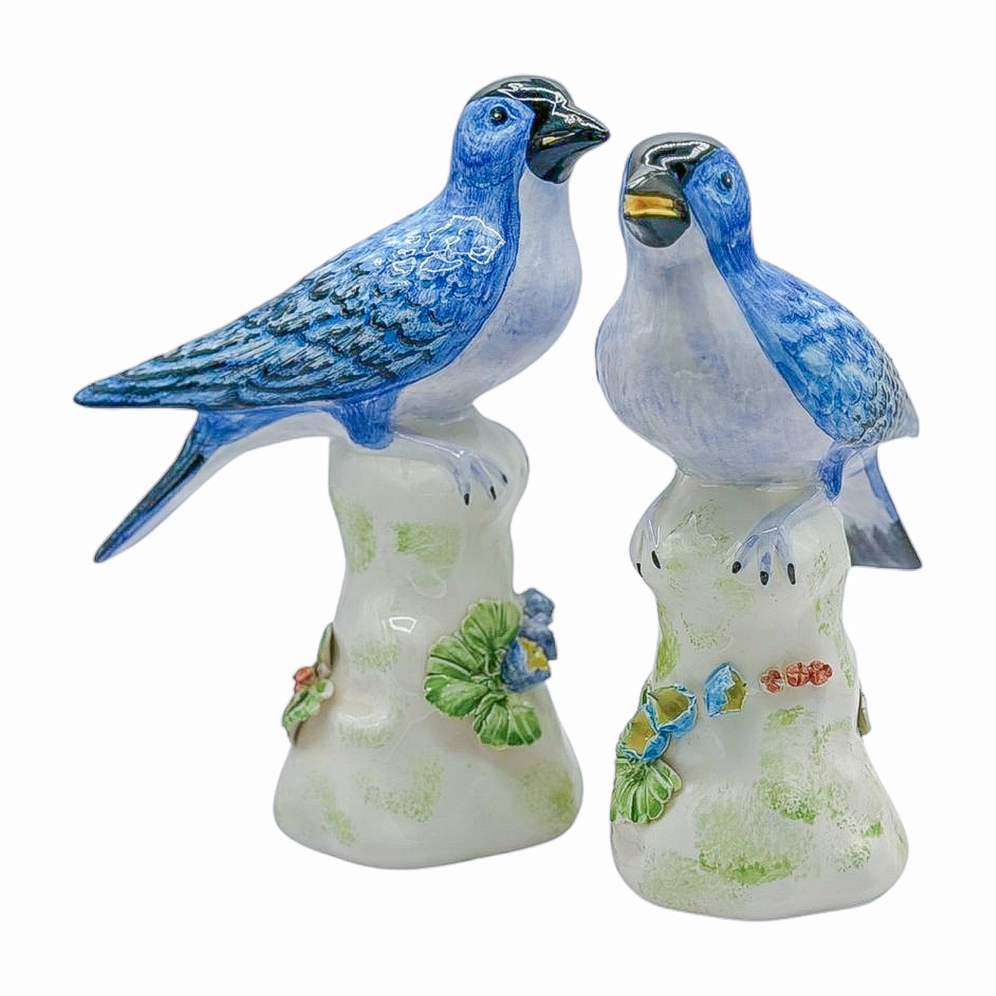 A pair worth chirping about. These painted Chelsea House birds sit perched atop delicate leafy bases, rendered in soft pastel tones with flashes of glossy cobalt. Equal parts elegant and cheeky—they make any tabletop, bookshelf, or vanity a bit more