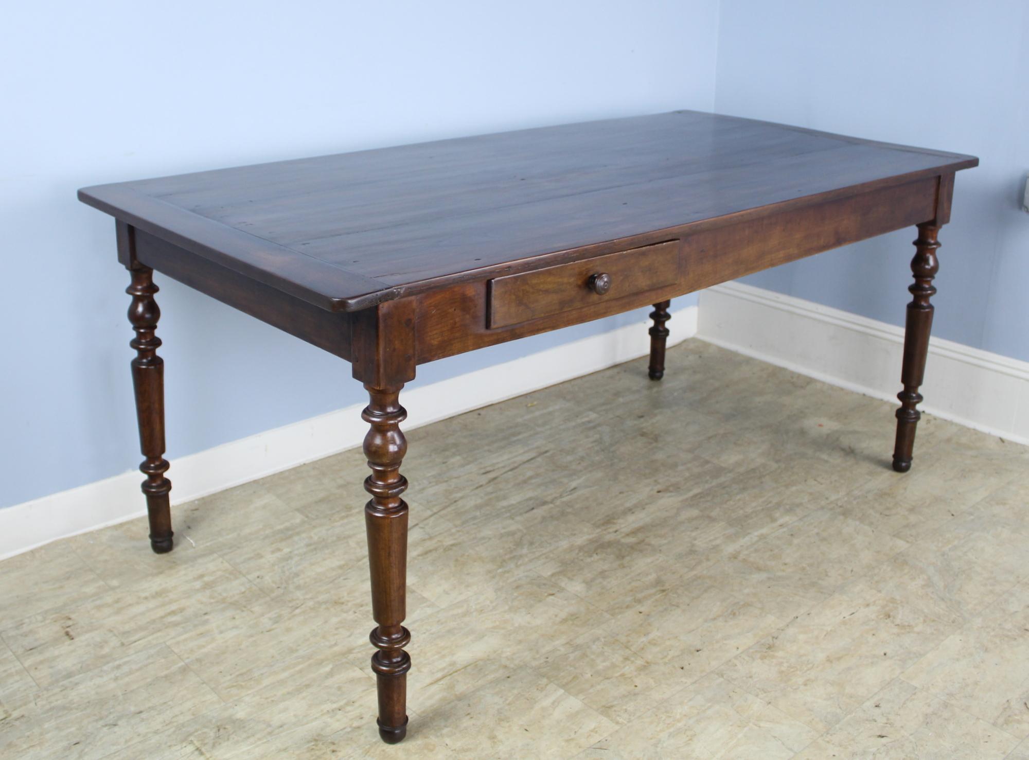 A smaller cherry farm table with glossy turned legs and a gently refinished top with breadboard ends. There is a one corner where the breadboard has warped slightly. Hardly noticeable and does not affect the utility of the table. Breadslide is in