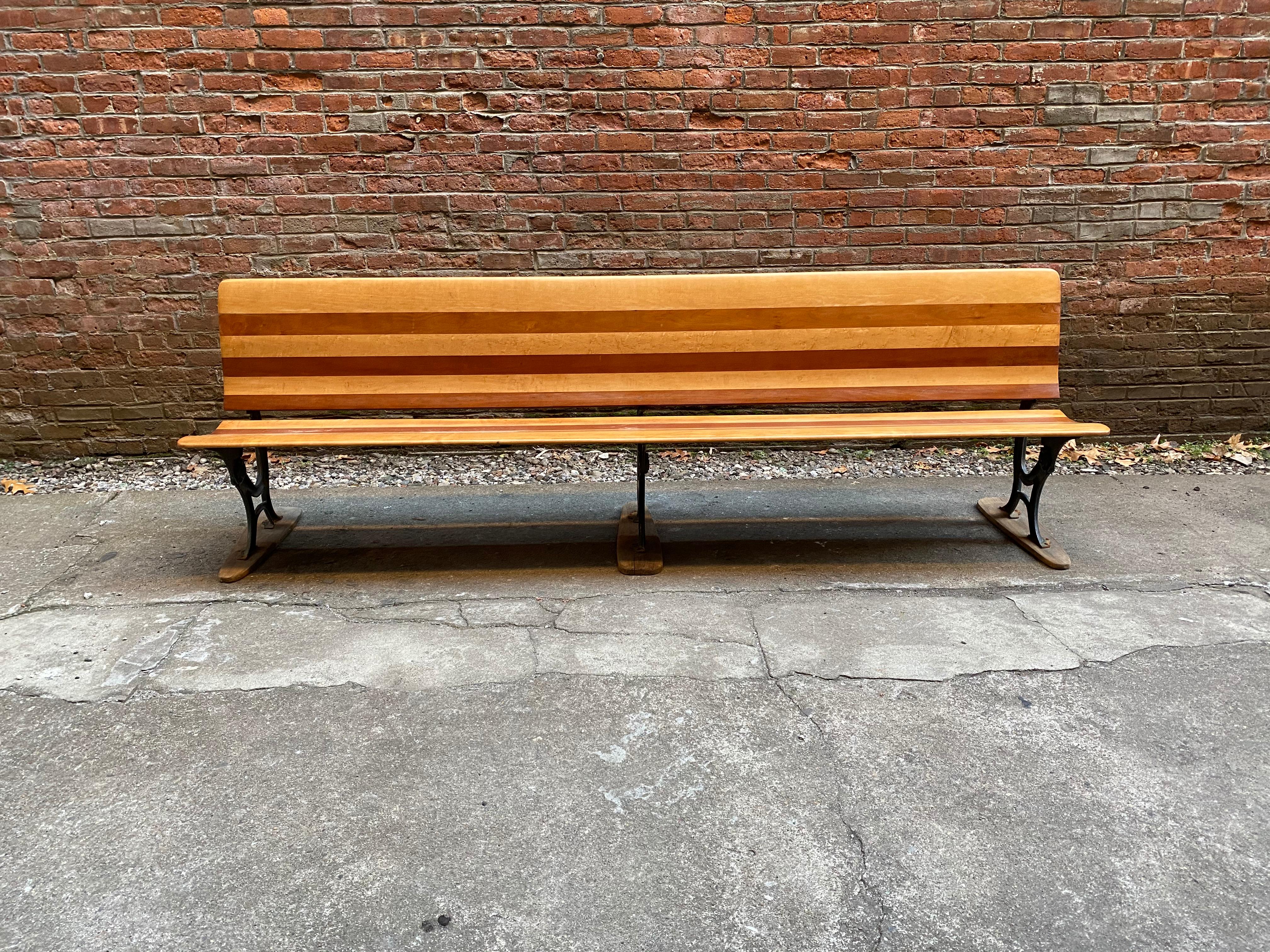 Cast iron base with folding seat and contoured back in cherry and maple. Eight feet of fantastic. The bench is perfect for the entrance or mudroom. The seat folds up. Originally used in a train depot. The feet were added by the previous owner, circa
