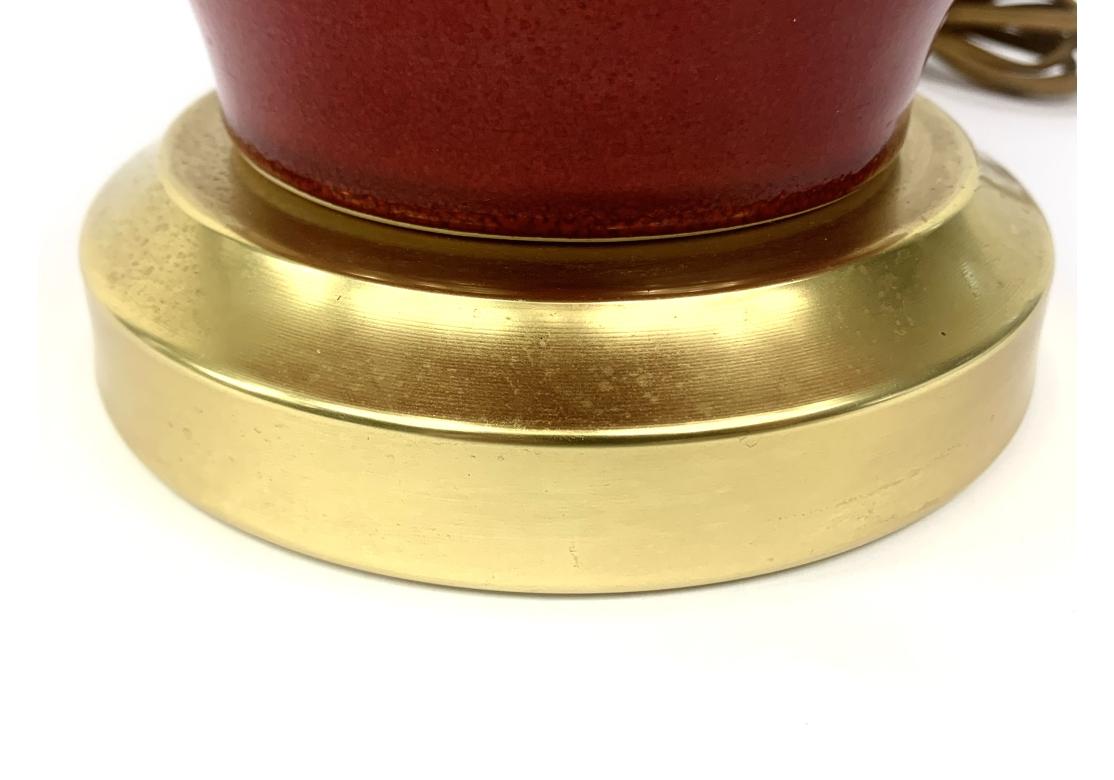 Une lampe de table du milieu du siècle, frappante et colorée, datant probablement des années 1960. Lampe vintage en céramique rouge cerise avec une forme de bouteille à long col, une base dorée, une harpe et un épi de faîtage