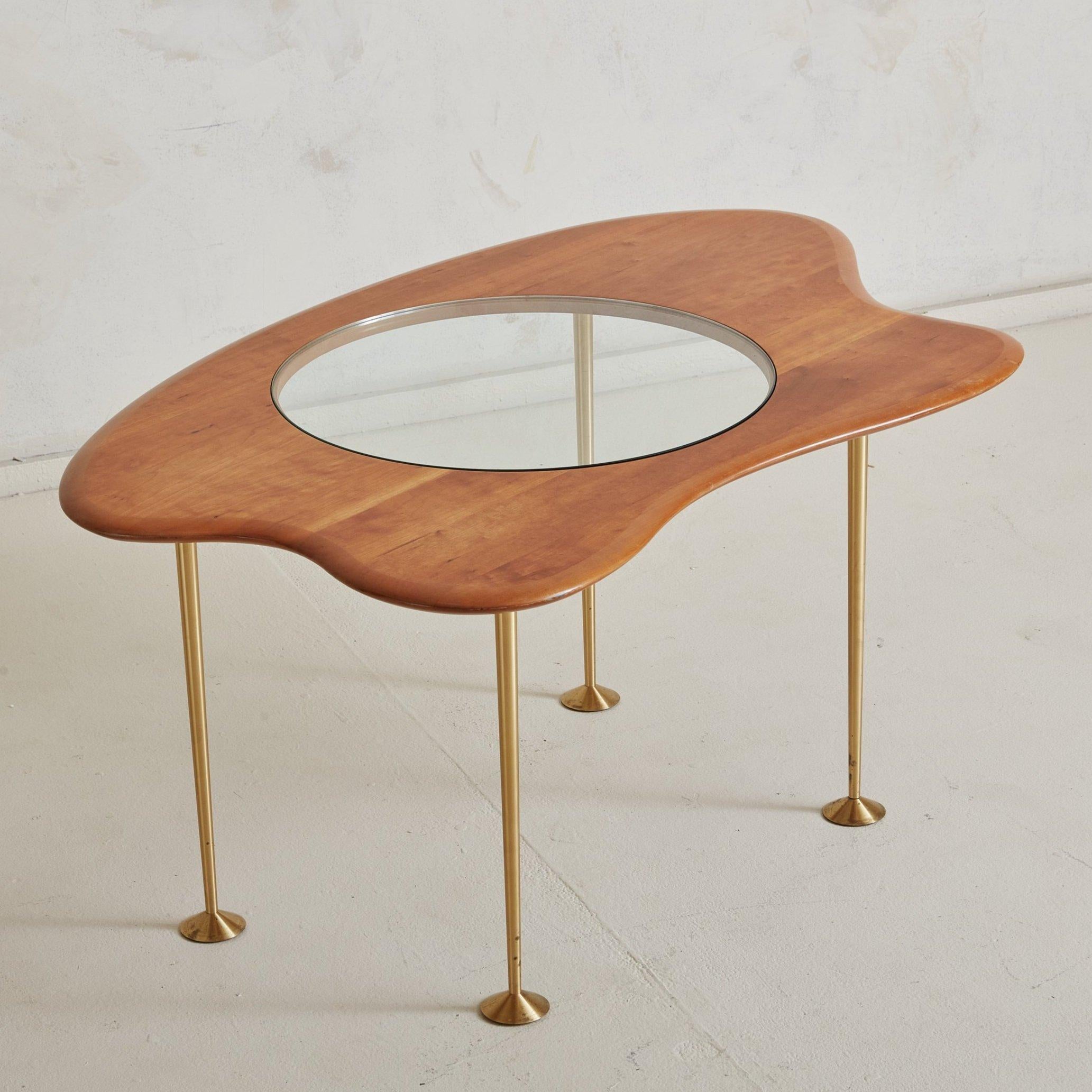 A rare Mid-Century Modern cherry wood, glass and brass coffee table. This coffee table features a stunning oblong shaped cherry wood top with horizontal graining and a seamlessly inset sheet of round transparent glass. Four minimalistic tapered