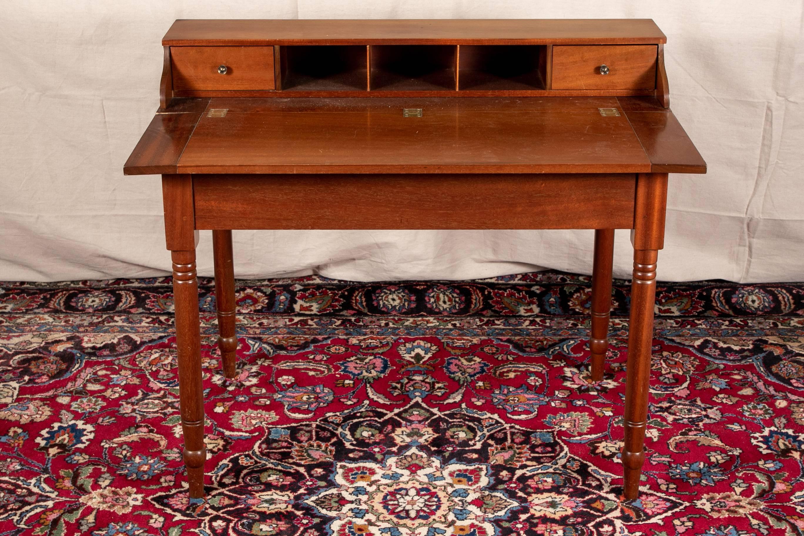 Cherry writing desk with three open compartments flanked by two small side drawers, turned cylindrical legs, terminating in topi feet, top with breadboard sides and lifts to reveal full compartment storage, label inside reads, 