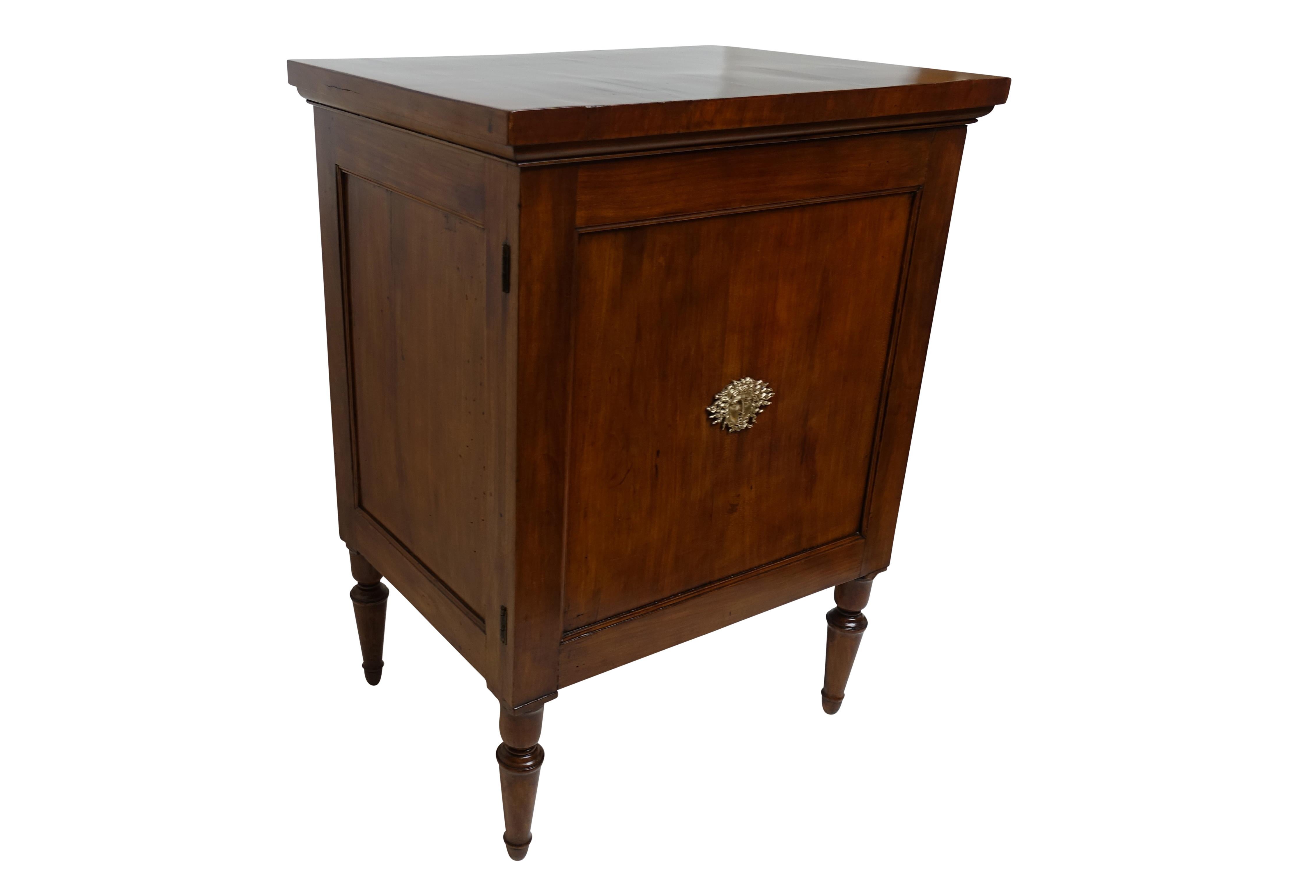 A cherrywood bedside cabinet with a brass applique on the centre of the door, two interior shelves (not original) and having an uncommon spring door release on the side, France, late 18th-early 19th century.