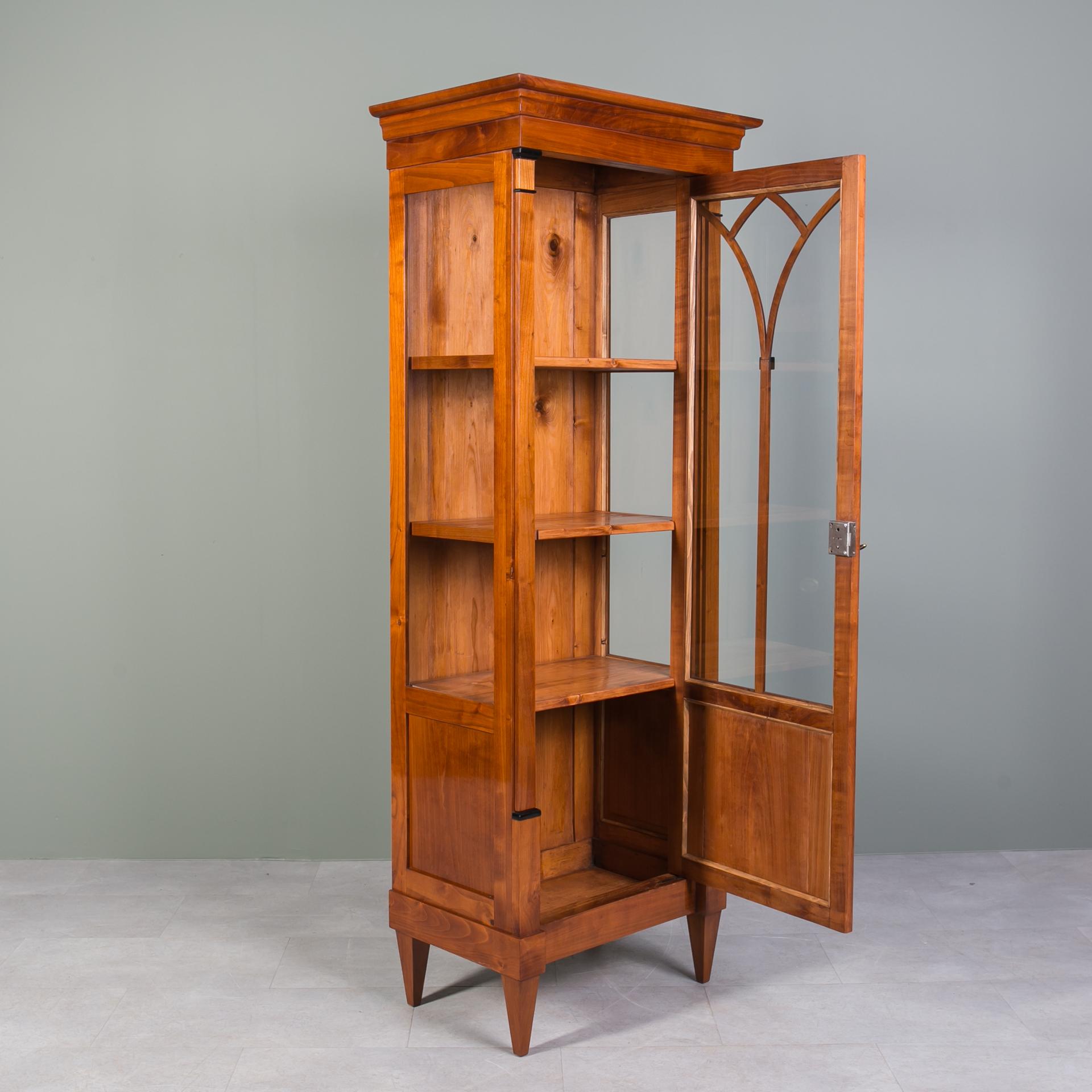 This beautiful vitrine comes from Germany and was made in 19th century, the Biedermeier period, showcasing a craftsmanship that stands the test of time. The construction is made of solid cherrywood. Behind the single door lockable with a key you