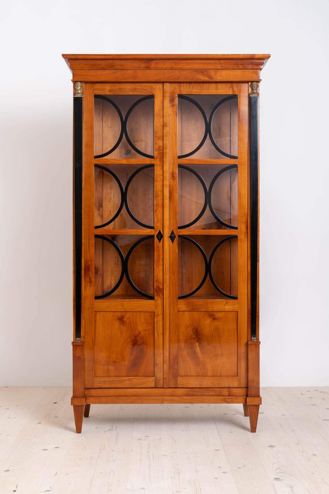 This beautiful vitrine comes from Germany and was made in 19th century, the Biedermeier period, showcasing a craftsmanship that stands the test of time.  The construction is made of solid cherrywood. Behind the doors lockable with a key you will