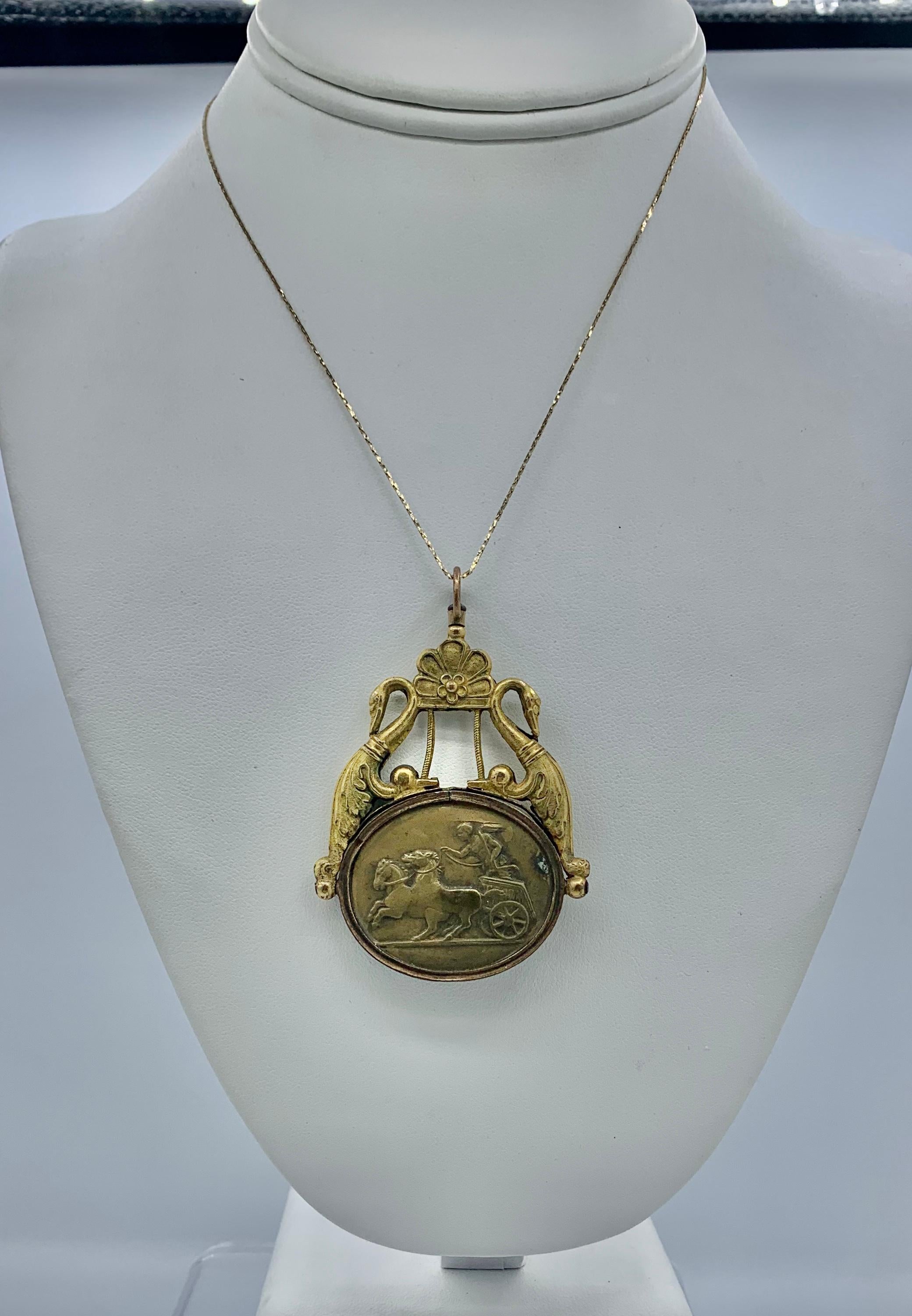 This is a magnificent rare early pendant with a bronze medallion of an Angel or Cherub riding in a chariot pulled by two horses. The medallion has a gold filled surmount with two swans on either side with acanthus leaf motif wings.  The rare jewel